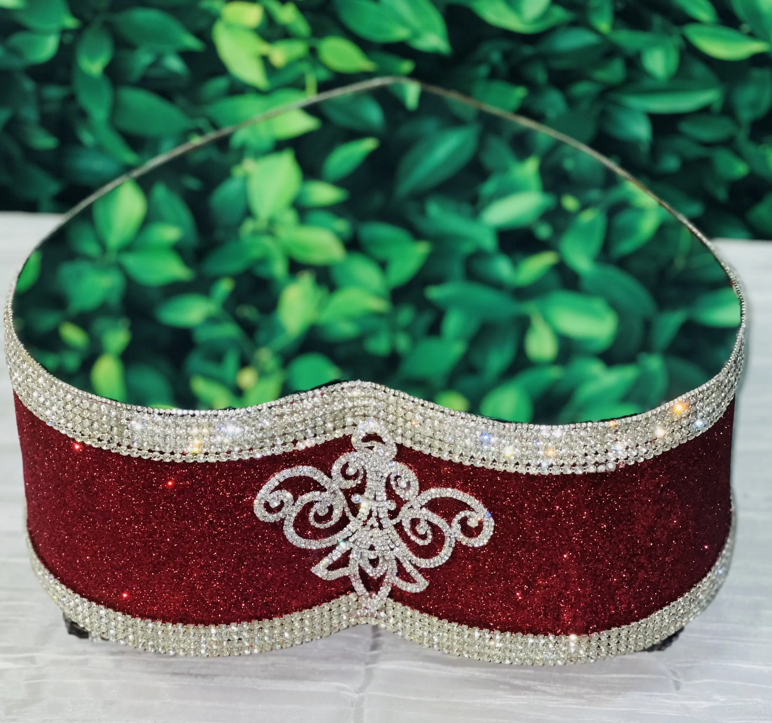 Heart-shaped mirror decorated with red glitter and rhinestones, reflecting green leaves.