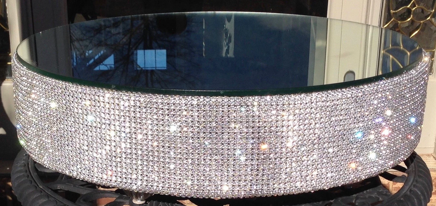 A round mirror with a frame encrusted with numerous small rhinestones, placed on a black tire.