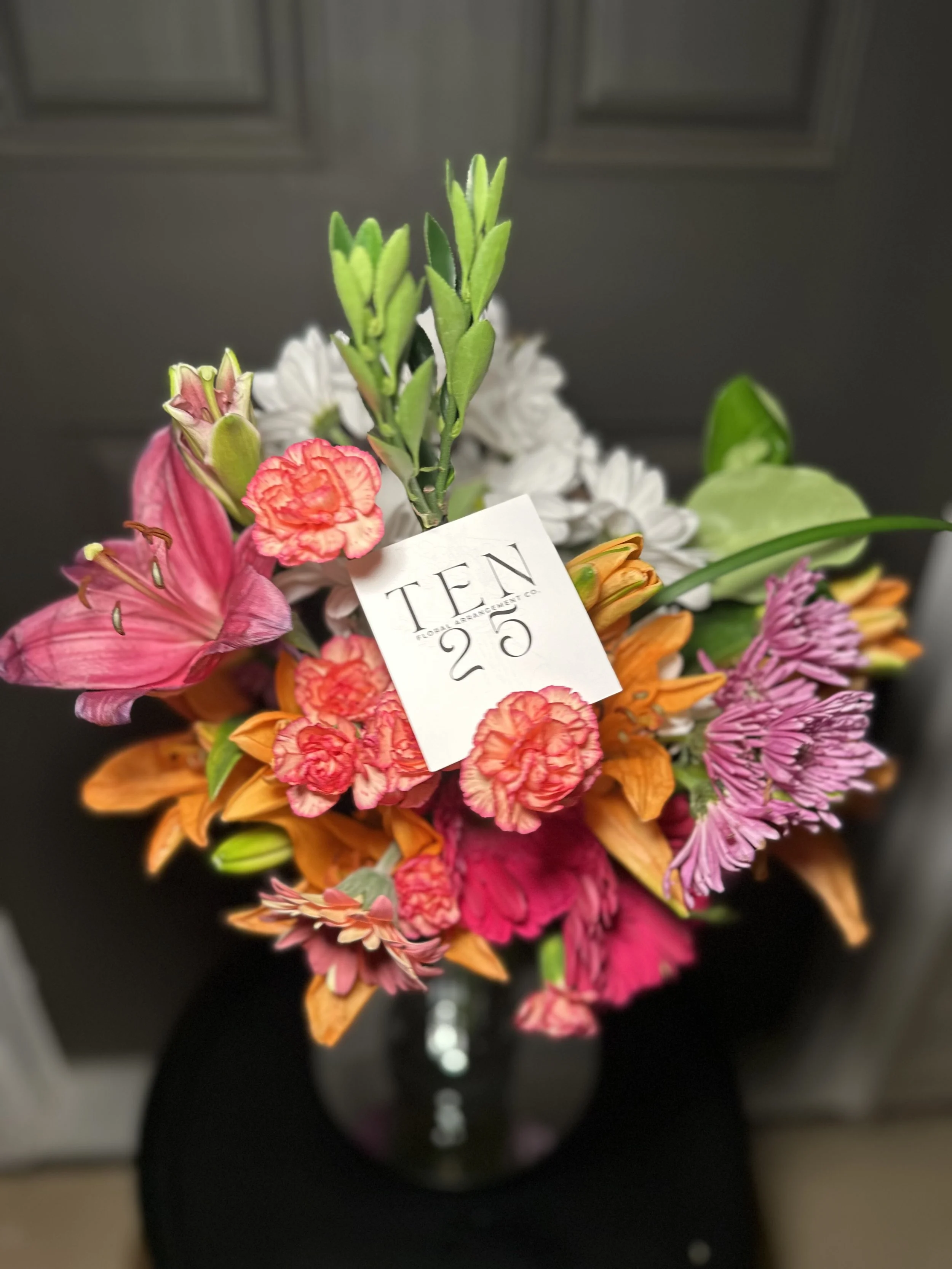 Colorful bouquet of flowers in a glass vase with a price tag that reads 'TEN 25' placed in the middle of the bouquet.
