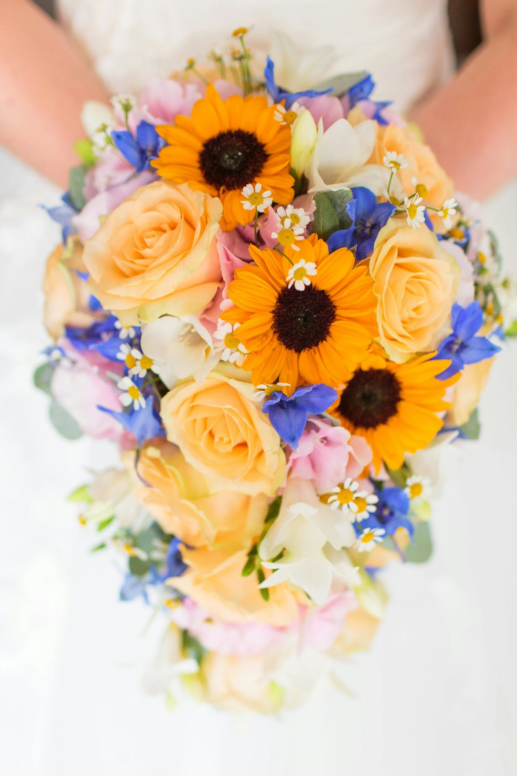 A bouquet of various colorful flowers including yellow roses, orange sunflowers, white flowers, blue flowers, and small white daisies.