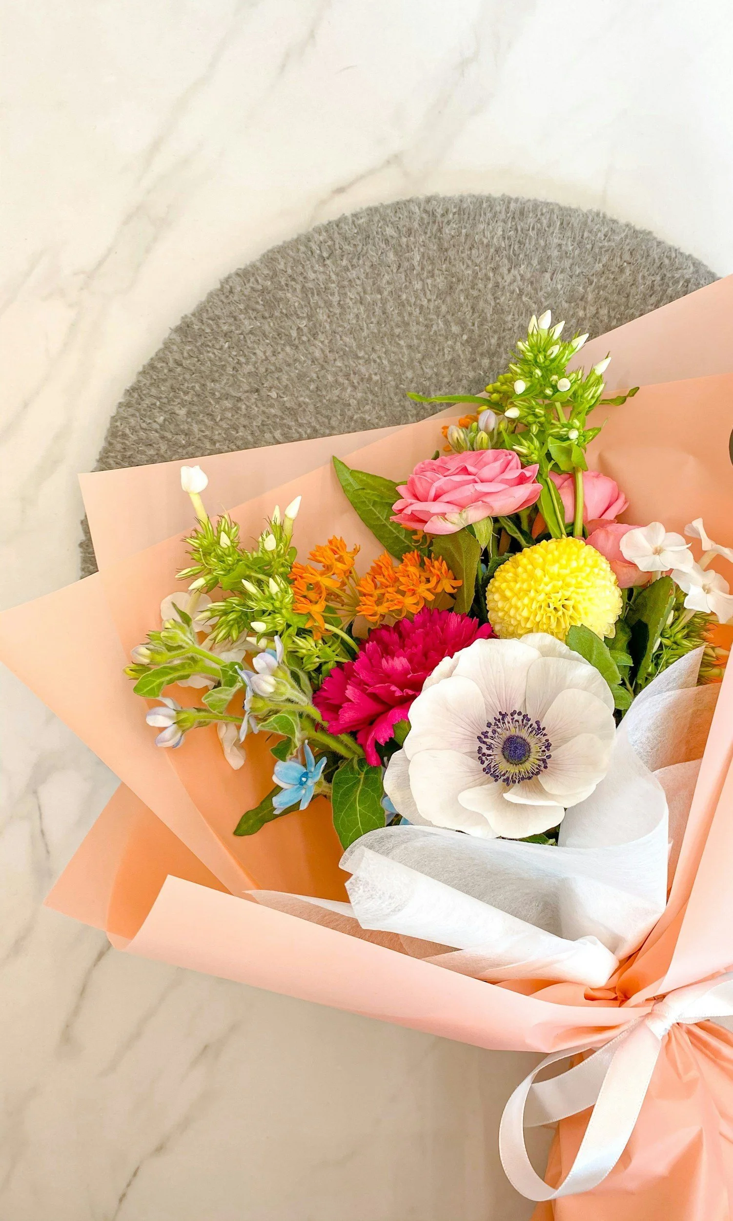 Colorful bouquet of mixed flowers wrapped in pink paper, placed on a gray textured surface.