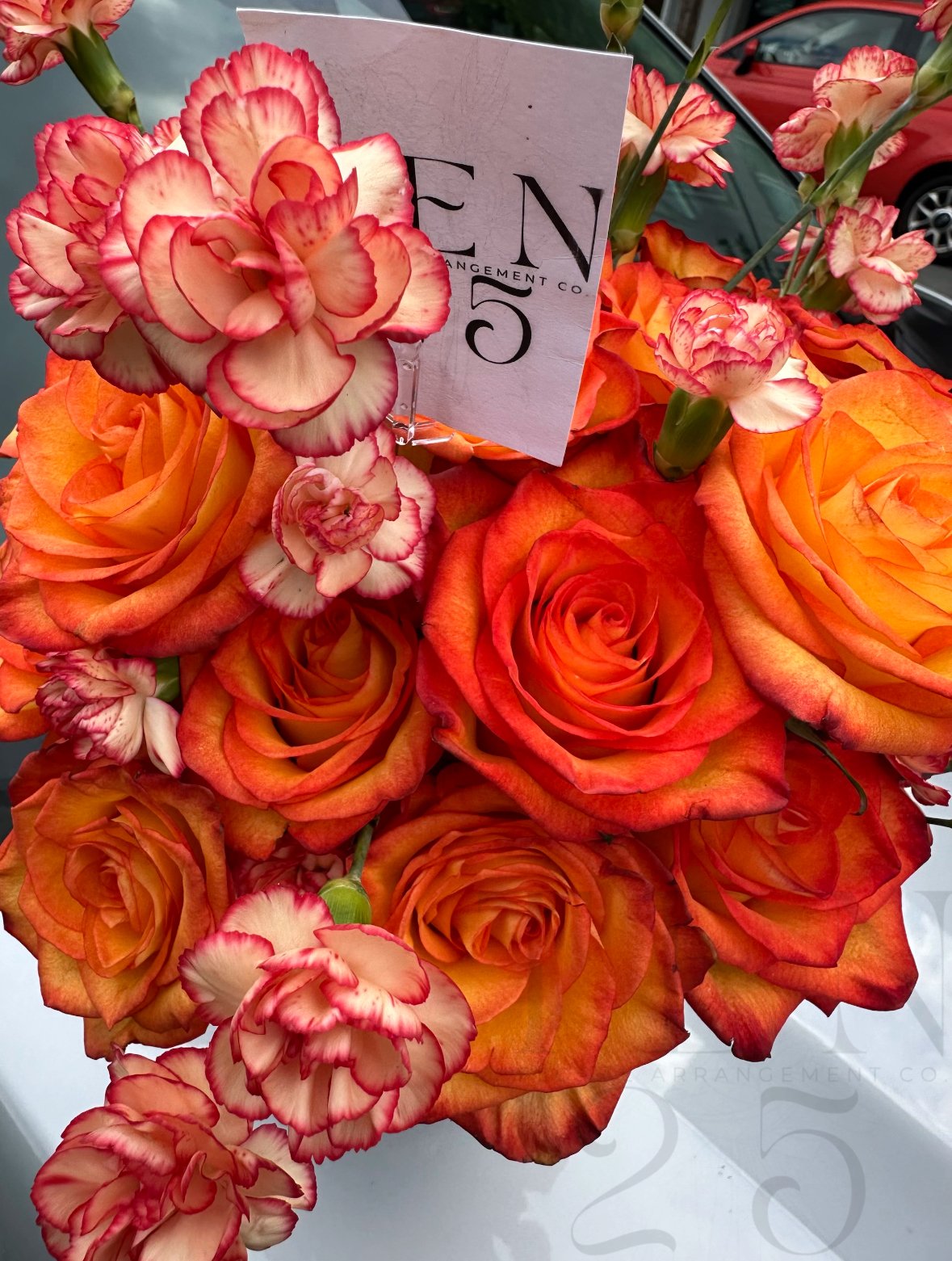 A bouquet of orange and peach roses with pink and white carnations, and a card with the partial text 'EN' and '5' in black lettering.