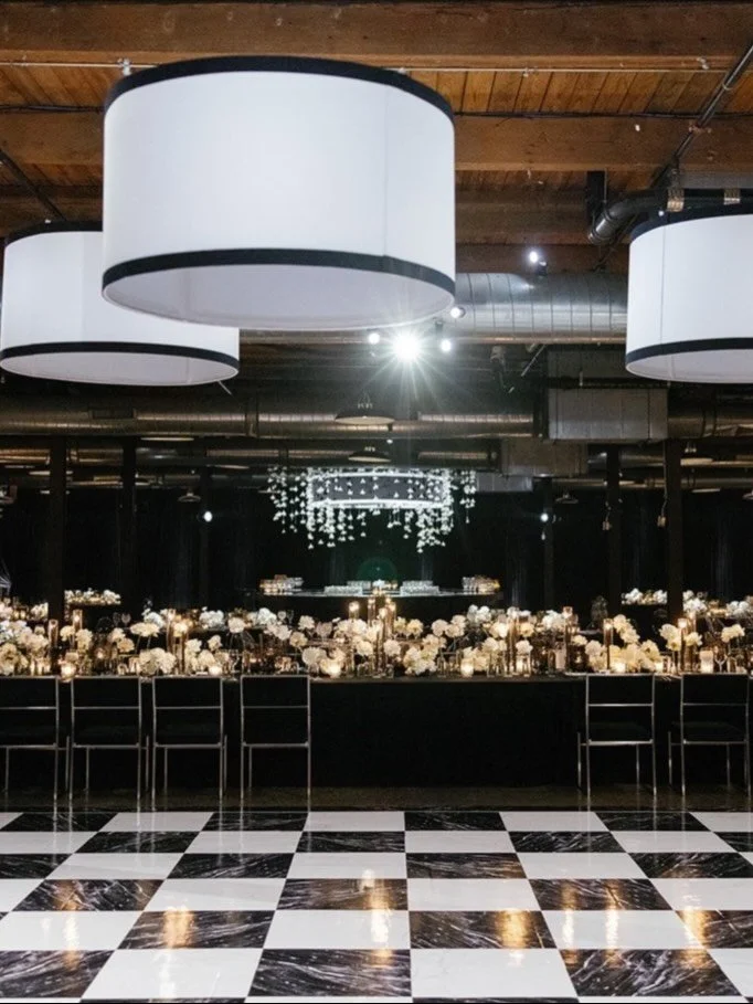 When a couple knows what they want, you listen.

In this case, it was a black-and-white checkered dance floor. That single decision shaped the room. Custom drum shades hung from the ceiling, carrying the geometry upward - extending the pattern withou