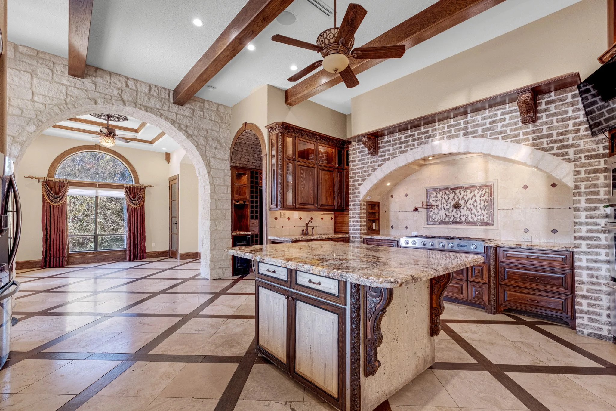 Kitchen with stone and brick walls, wooden cabinets, granite island, ceiling fan, and large window.