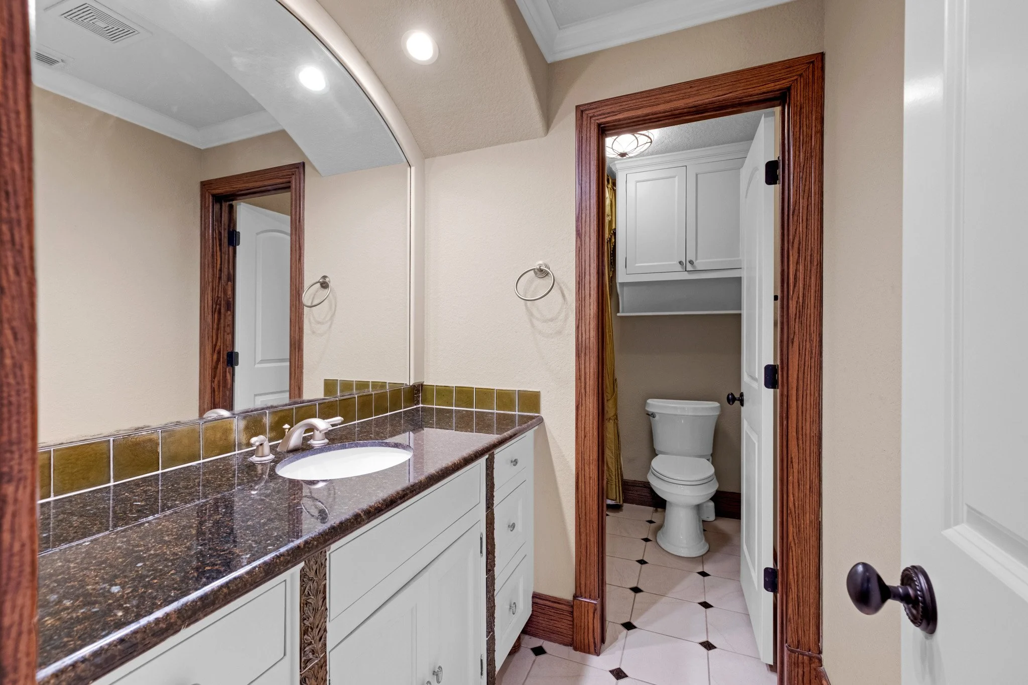 Bathroom with a large mirror, brown tile countertop, a sink, and a visible toilet behind a door.