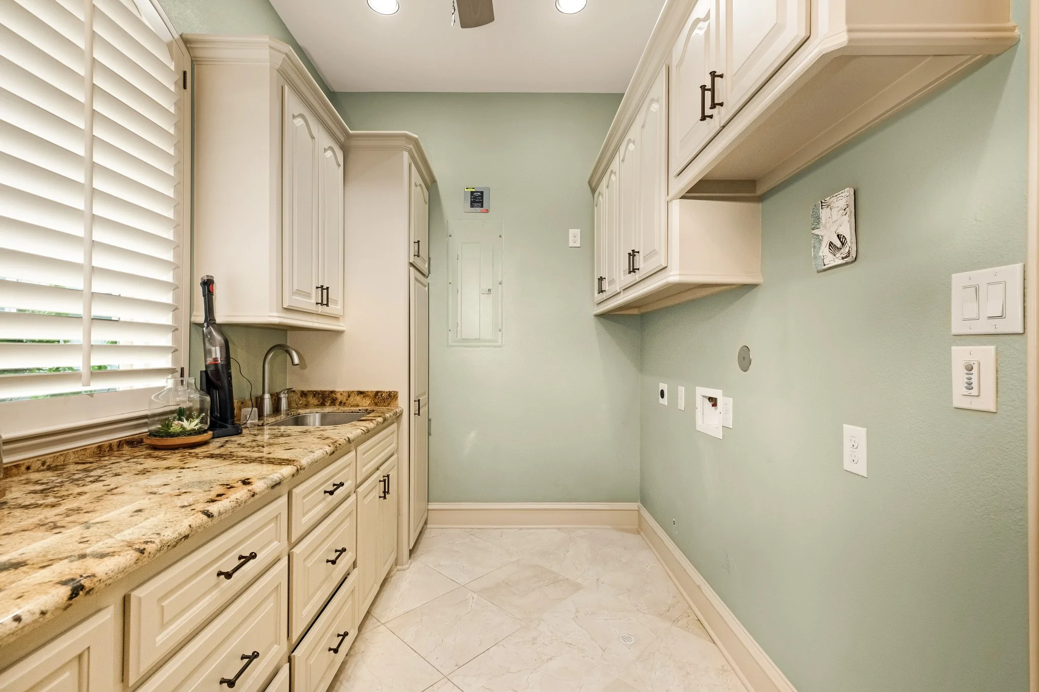 Empty kitchen laundry room with white cabinets, granite countertops, and a window with white shutters.