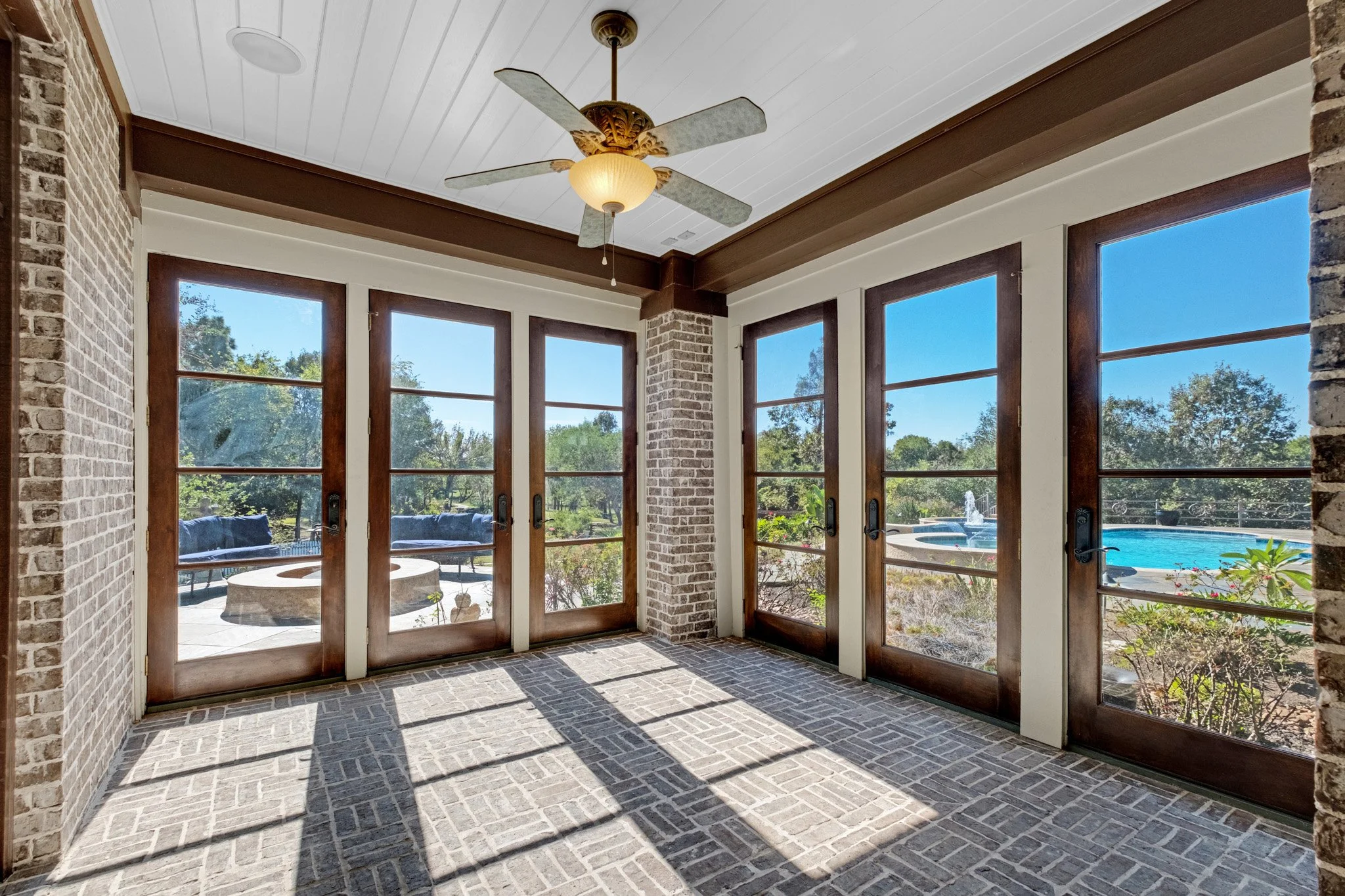 Sunroom with large glass doors, brick walls, ceiling fan, and views of a backyard with a swimming pool and outdoor seating.