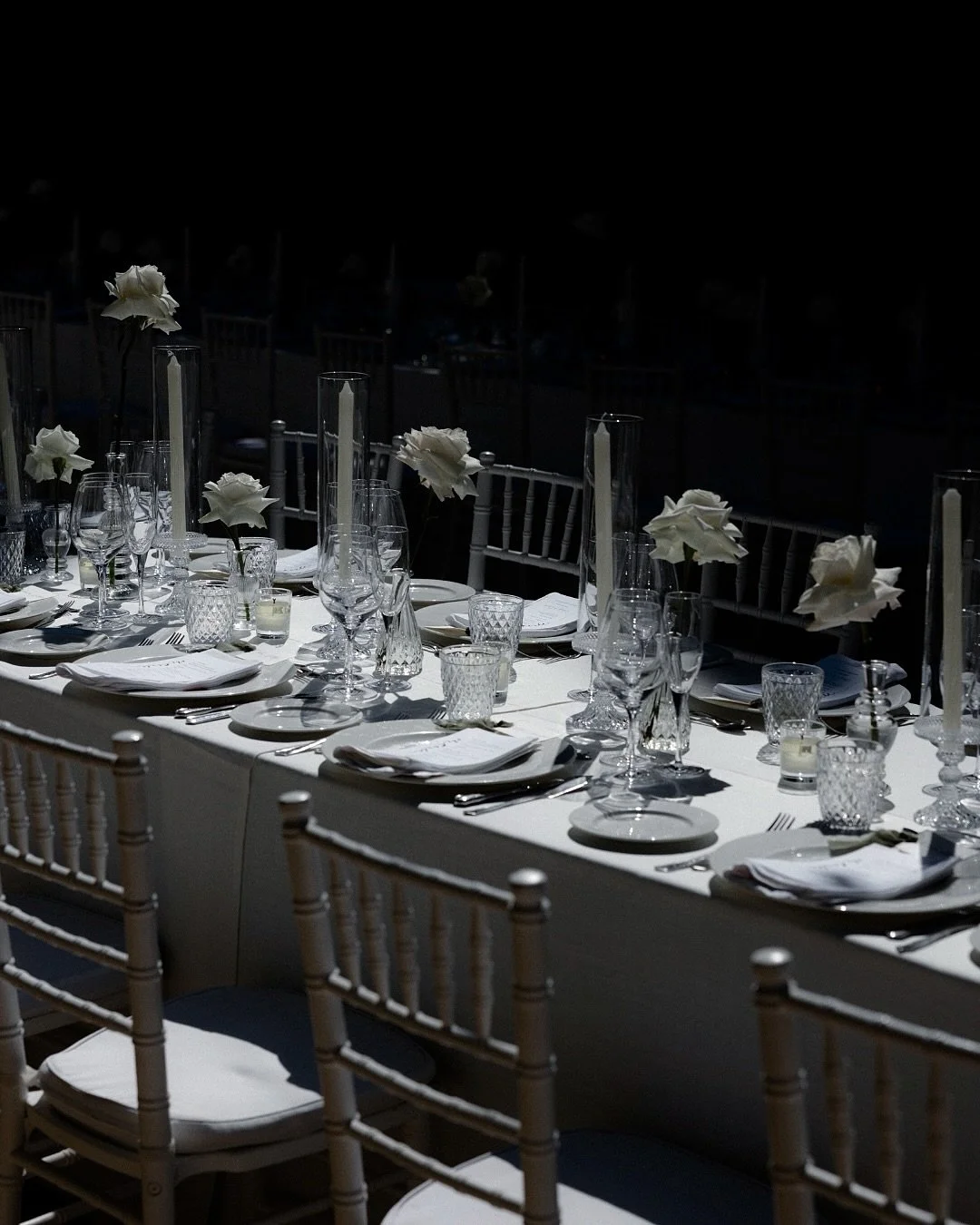 Una mesa imperial con rosas blancas y velas altas que proyectaban sombras perfectas sobre el mantel.   Rosas blancas en jarrones de cristal soplado, velas altas, cristaler&iacute;a tallada y los nombres escritos a mano en cada men&uacute;. El tipo de