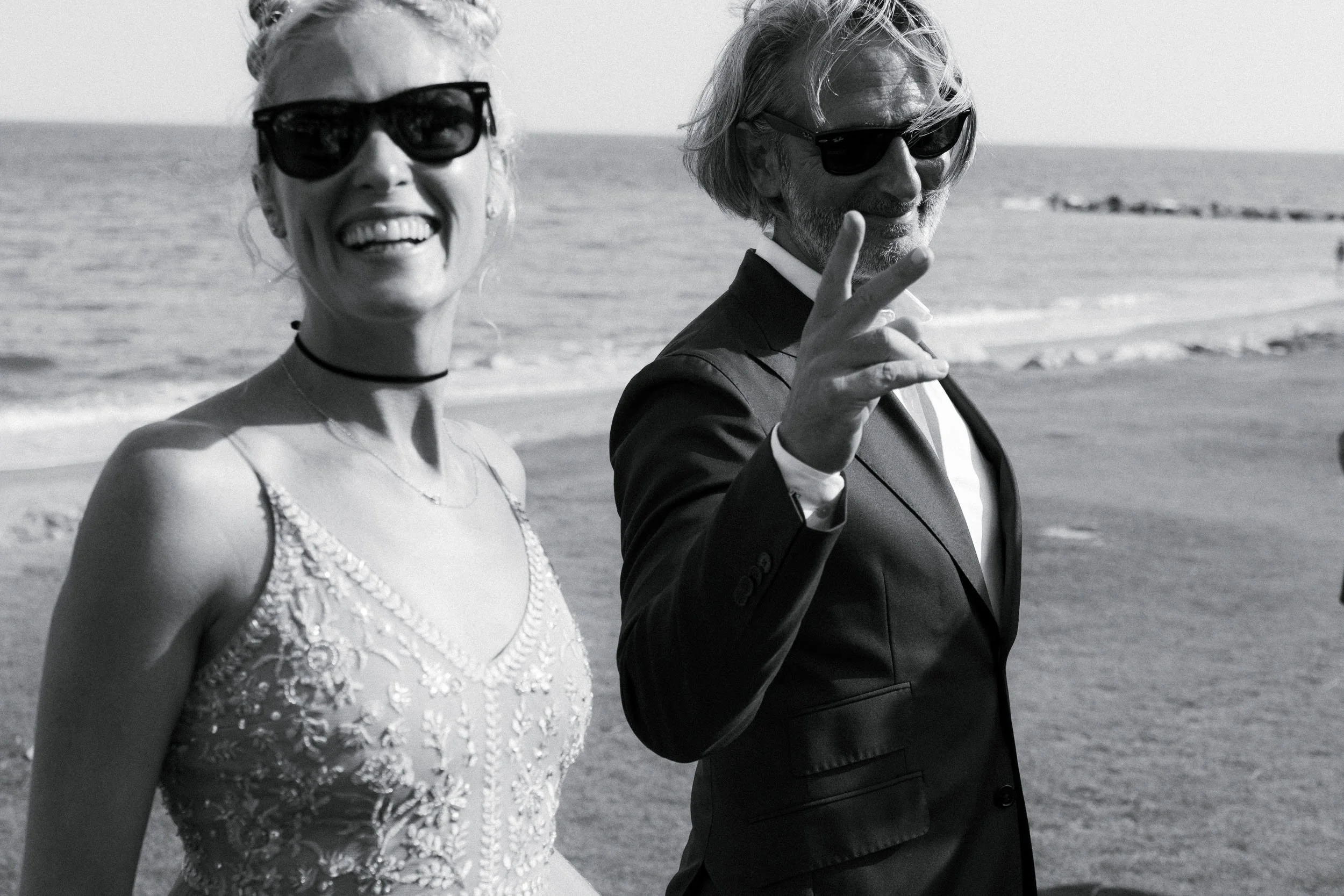 Novios disfrutando de un momento espontáneo y divertido con gafas de sol durante su boda en la playa en Sotogrande. Fotografía de boda natural y sin posados en blanco y negro que captura la actitud de la pareja.