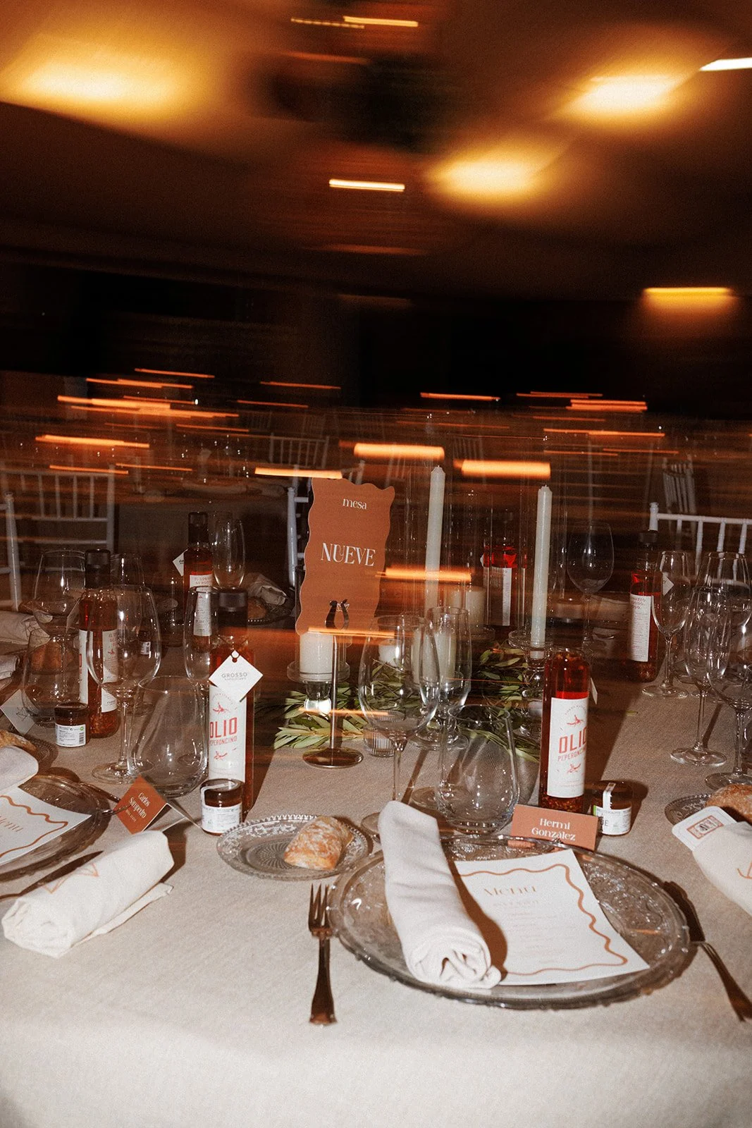 Detalles de mesa en una boda con botellas de aceite gourmet como regalo para invitados. Fotografía creativa con flash directo y movimiento para transmitir el ambiente festivo de la cena.