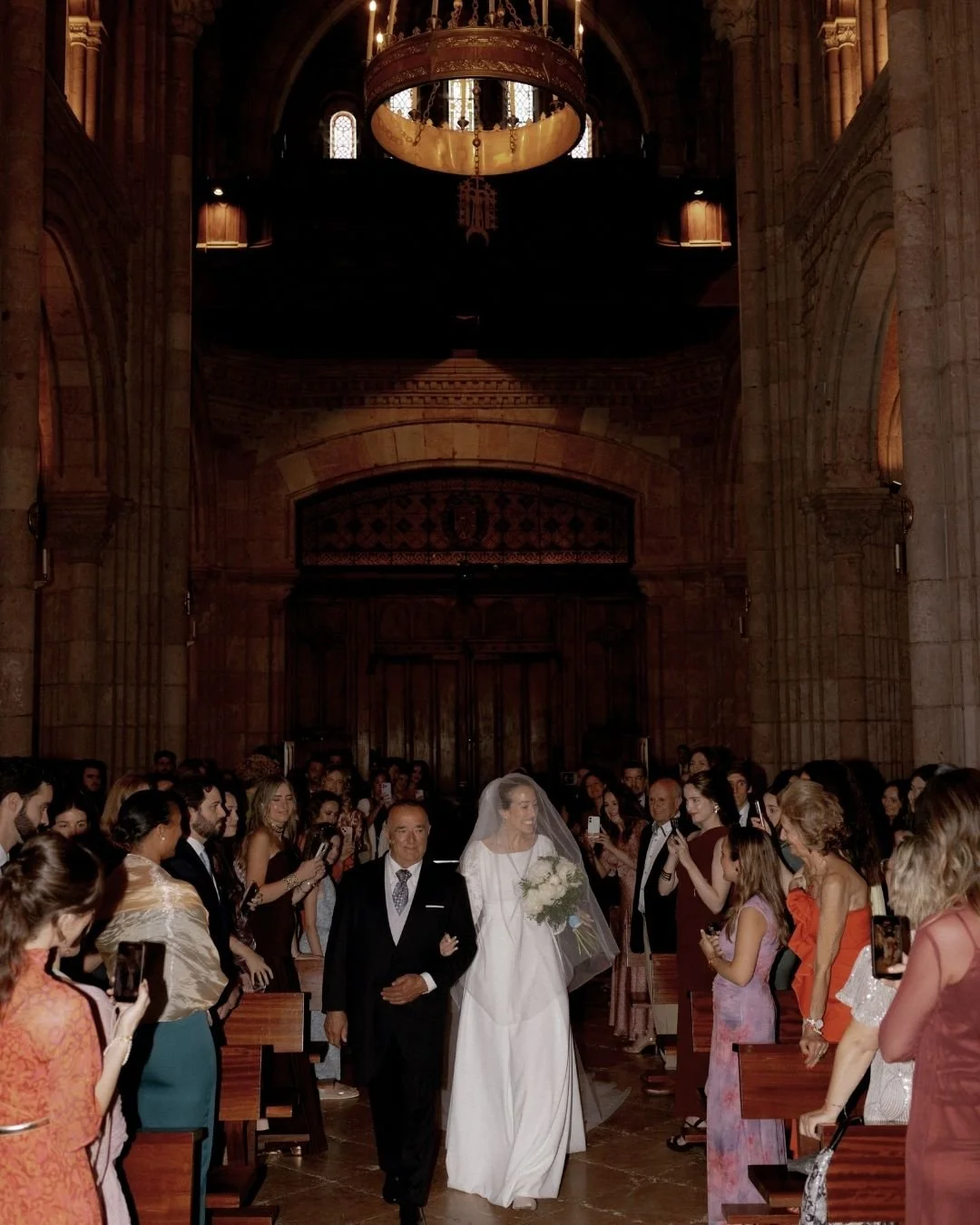 Novia caminando hacia el altar del brazo de su padrino en una iglesia impresionante. Imagen que refleja la solemnidad y emoción previa al "sí, quiero".
