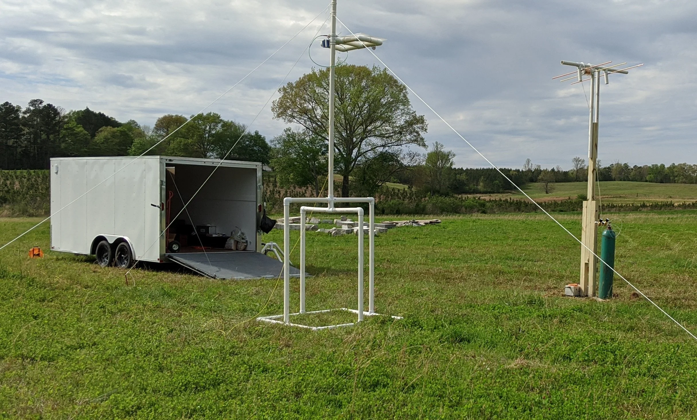 Two tall poles similar to electric poles in a grassy field with a covered trailer.