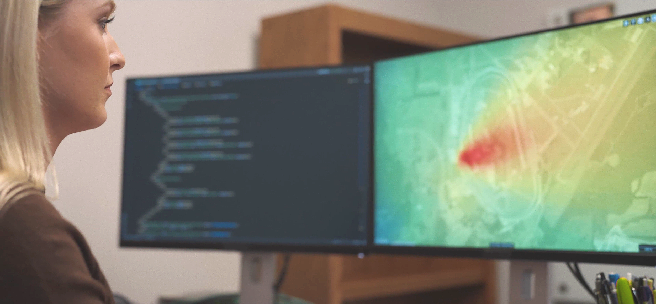 A woman sitting at a desk with two computer monitors.