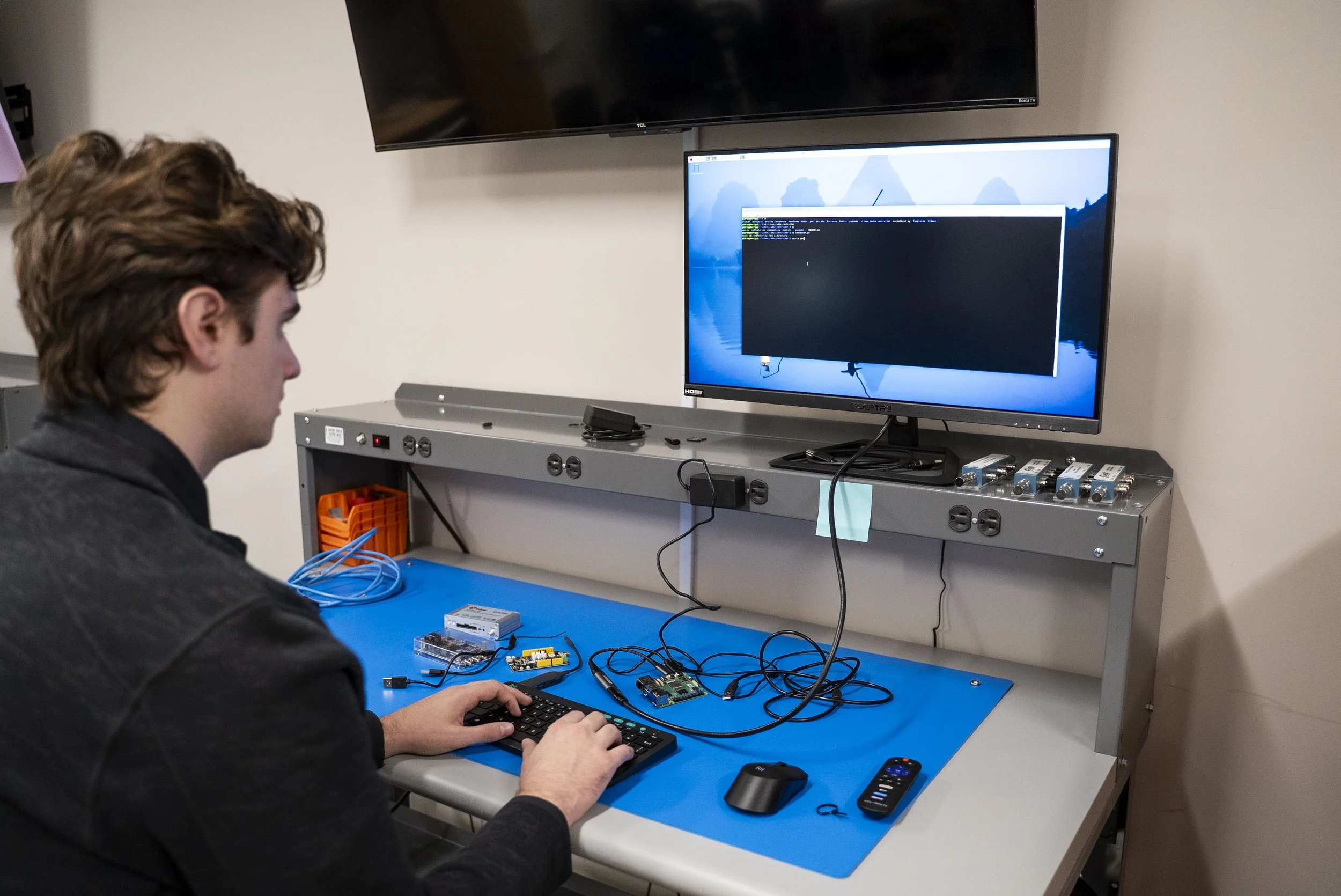 An over-the-shoulder shot of a man working at a desk with non-specific data on his computer monitors.