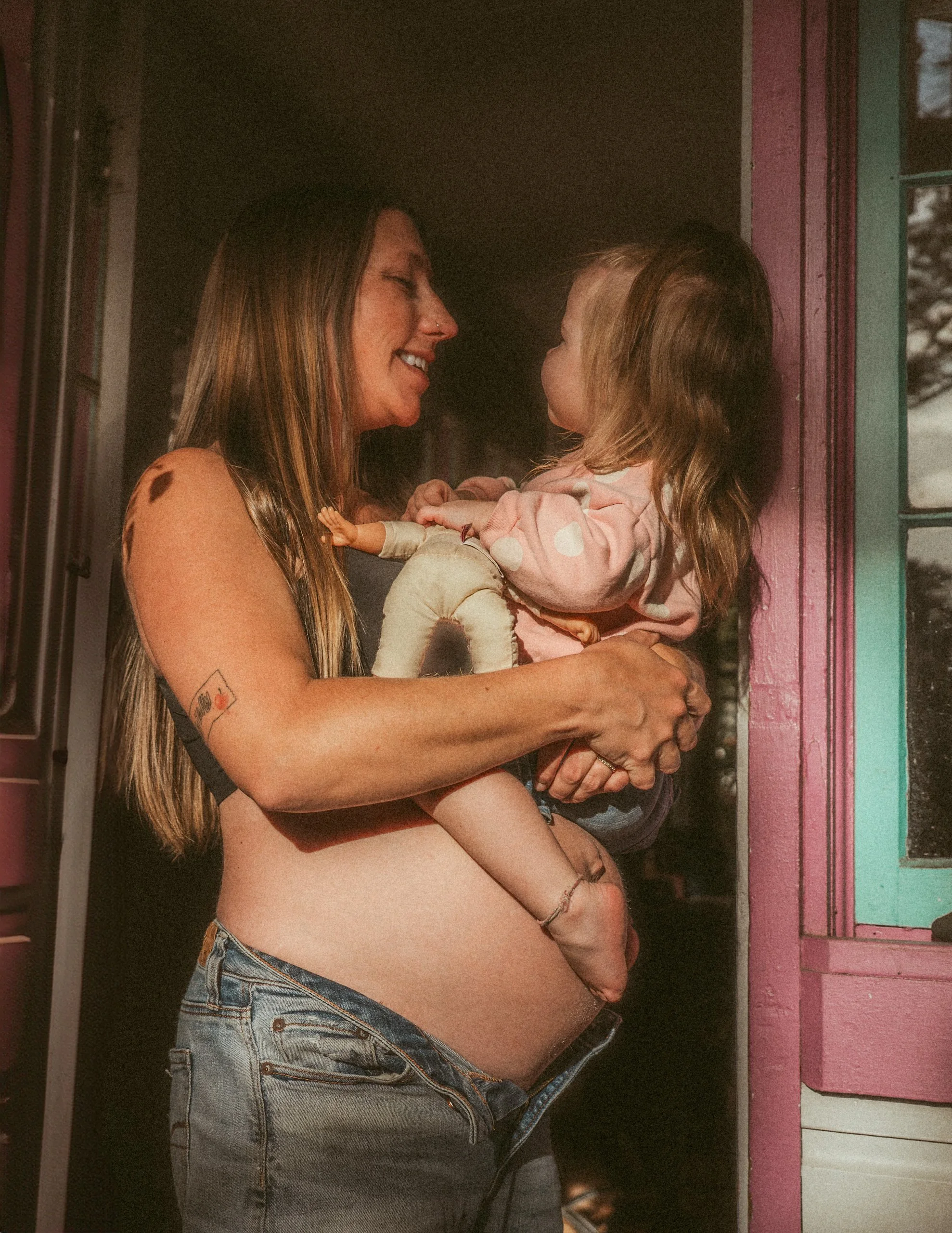 A woman holding a young girl in her arms, smiling and looking at each other through a window with a pink frame.