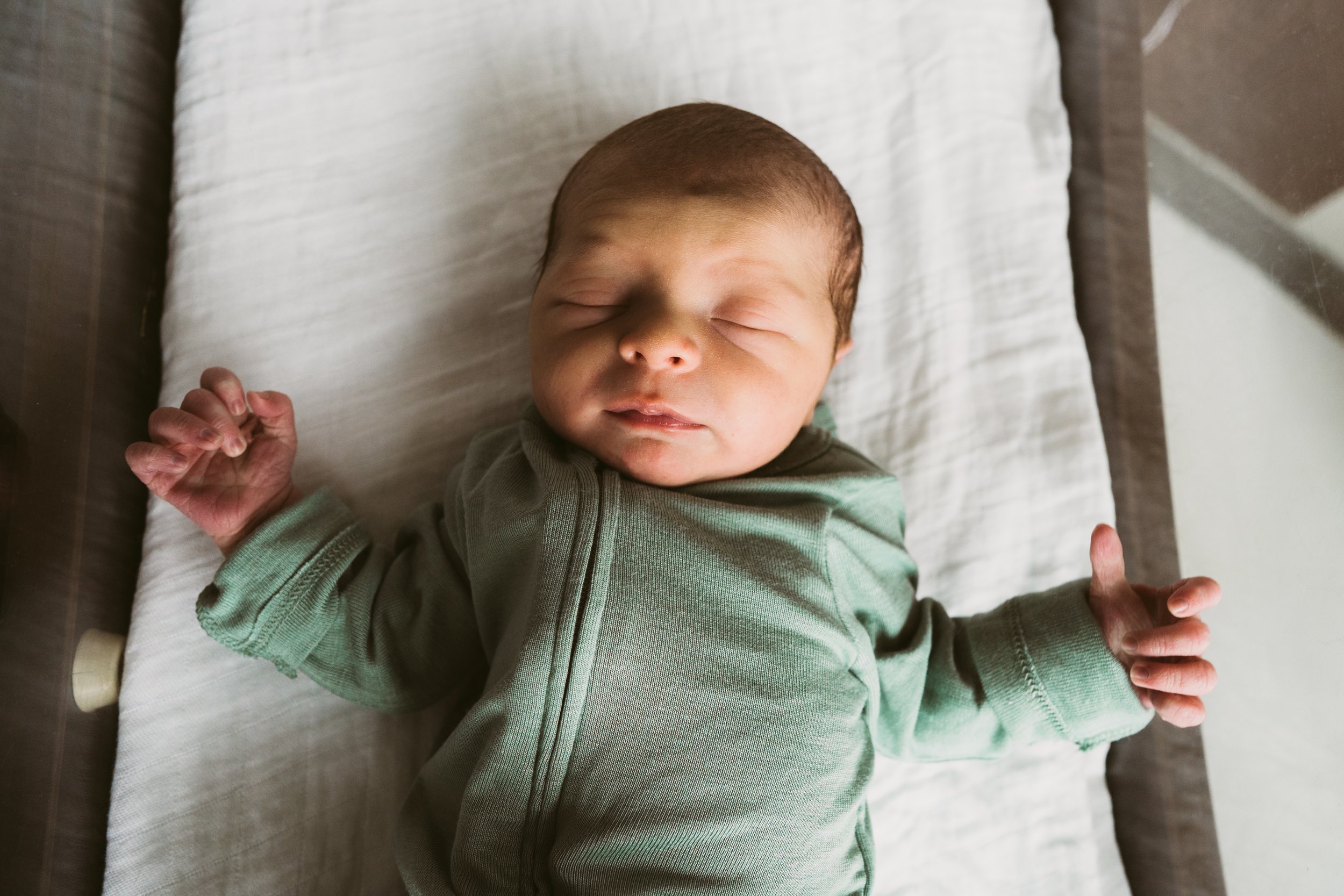 Close-up of a sleeping newborn baby lying on a pillow on a bed, with hands resting on the blanket.