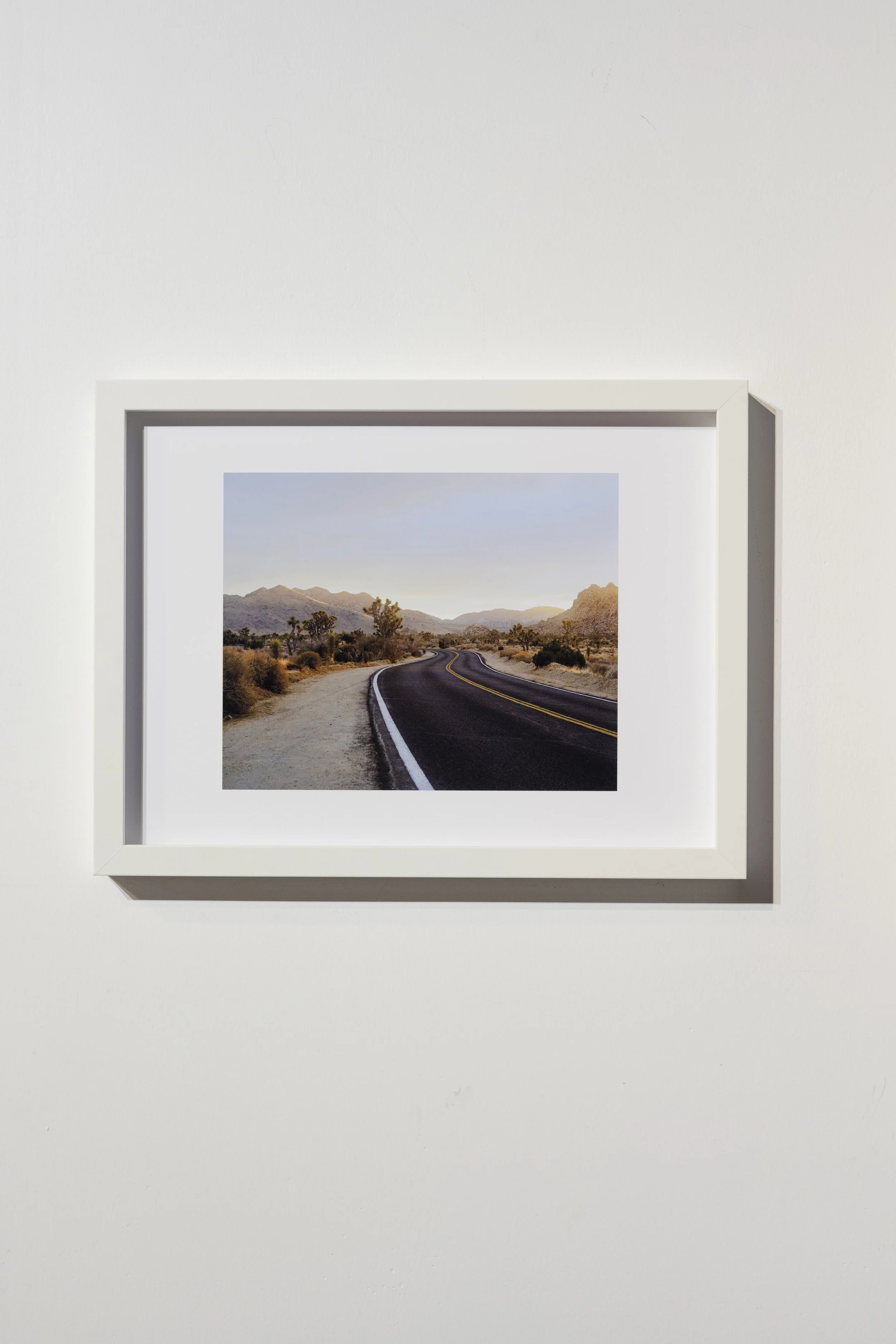 Une photographie encadrée d'une route de campagne sinueuse avec des montagnes en arrière-plan, prise lors d'un coucher de soleil dans un paysage désertique.