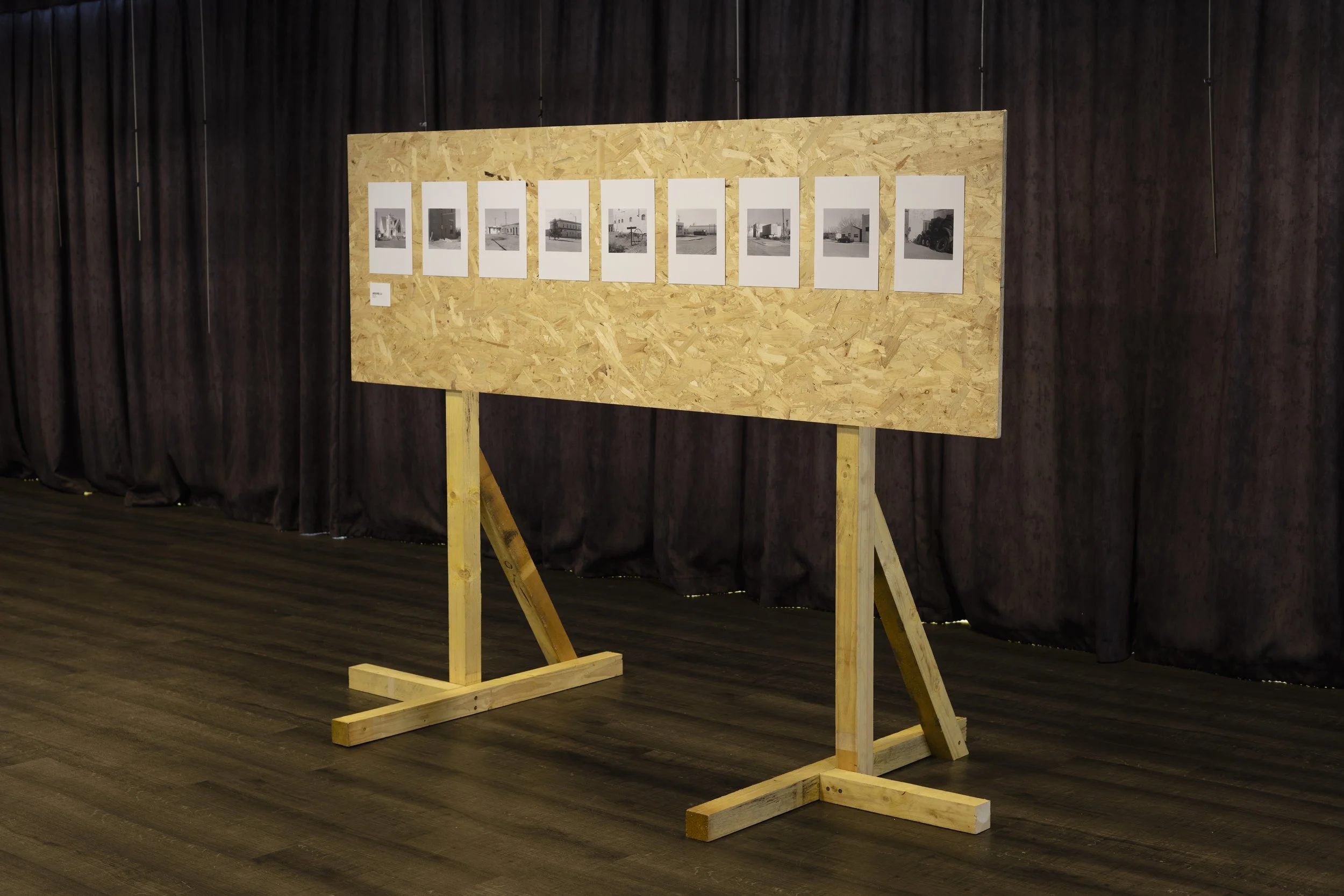 Une structure en bois avec des photographies en noir et blanc affichées, située dans une salle avec des rideaux sombres en fond.