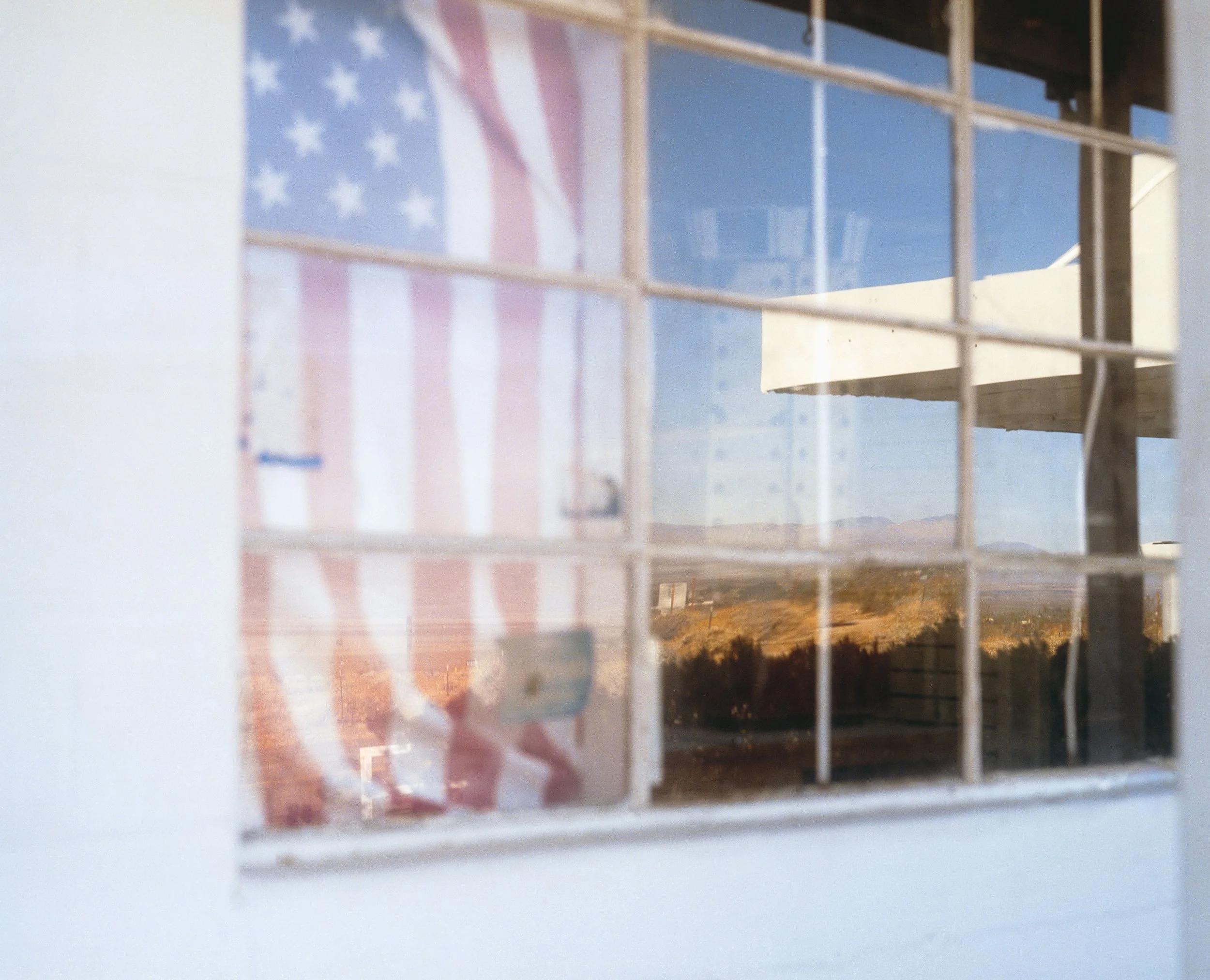 Reflet d'un drapeau américain dans une vitre avec un paysage montagneux au loin.