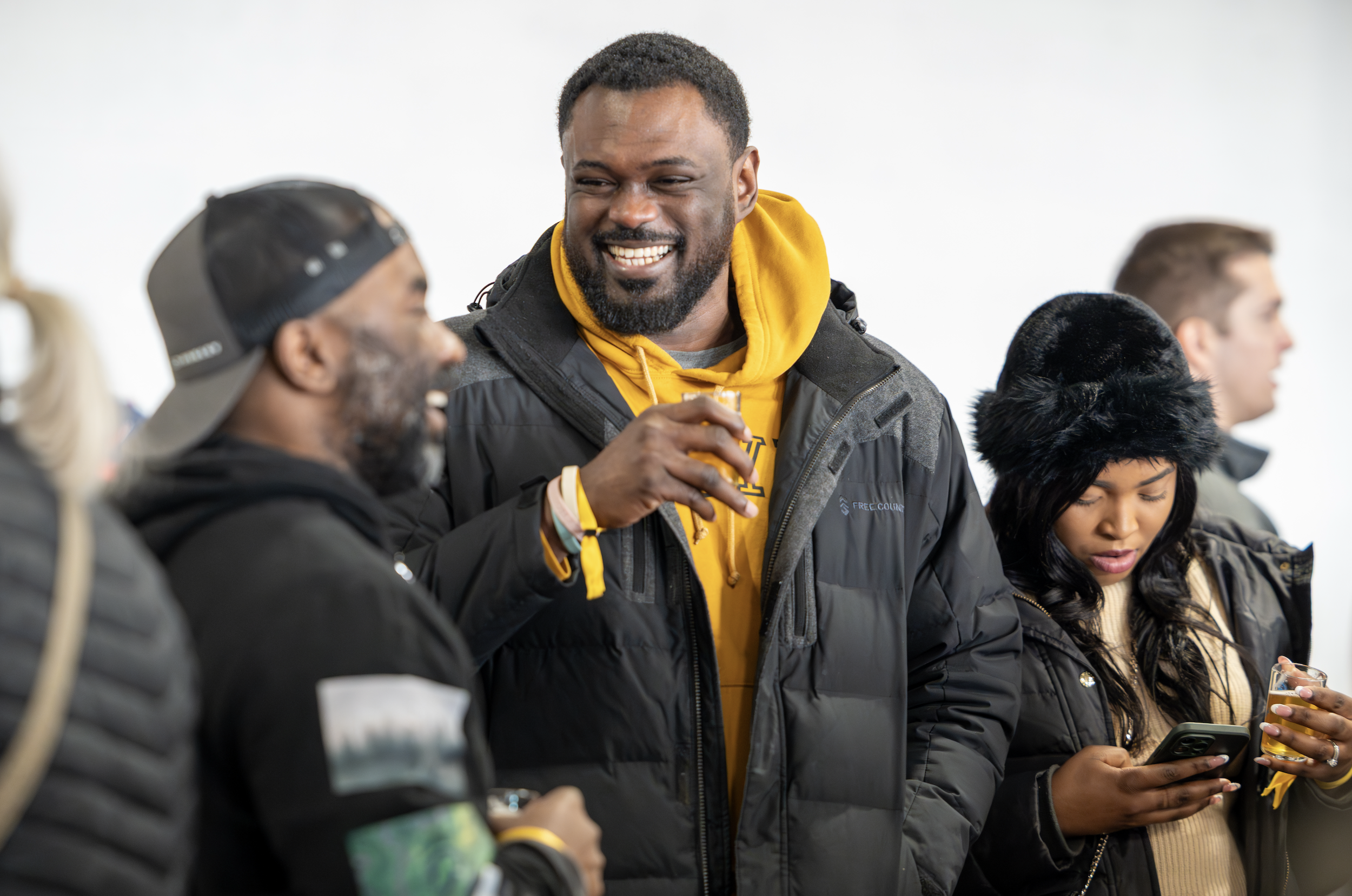 Group of attendees smiling and holding beer samples while socializing at an indoor beer festival.