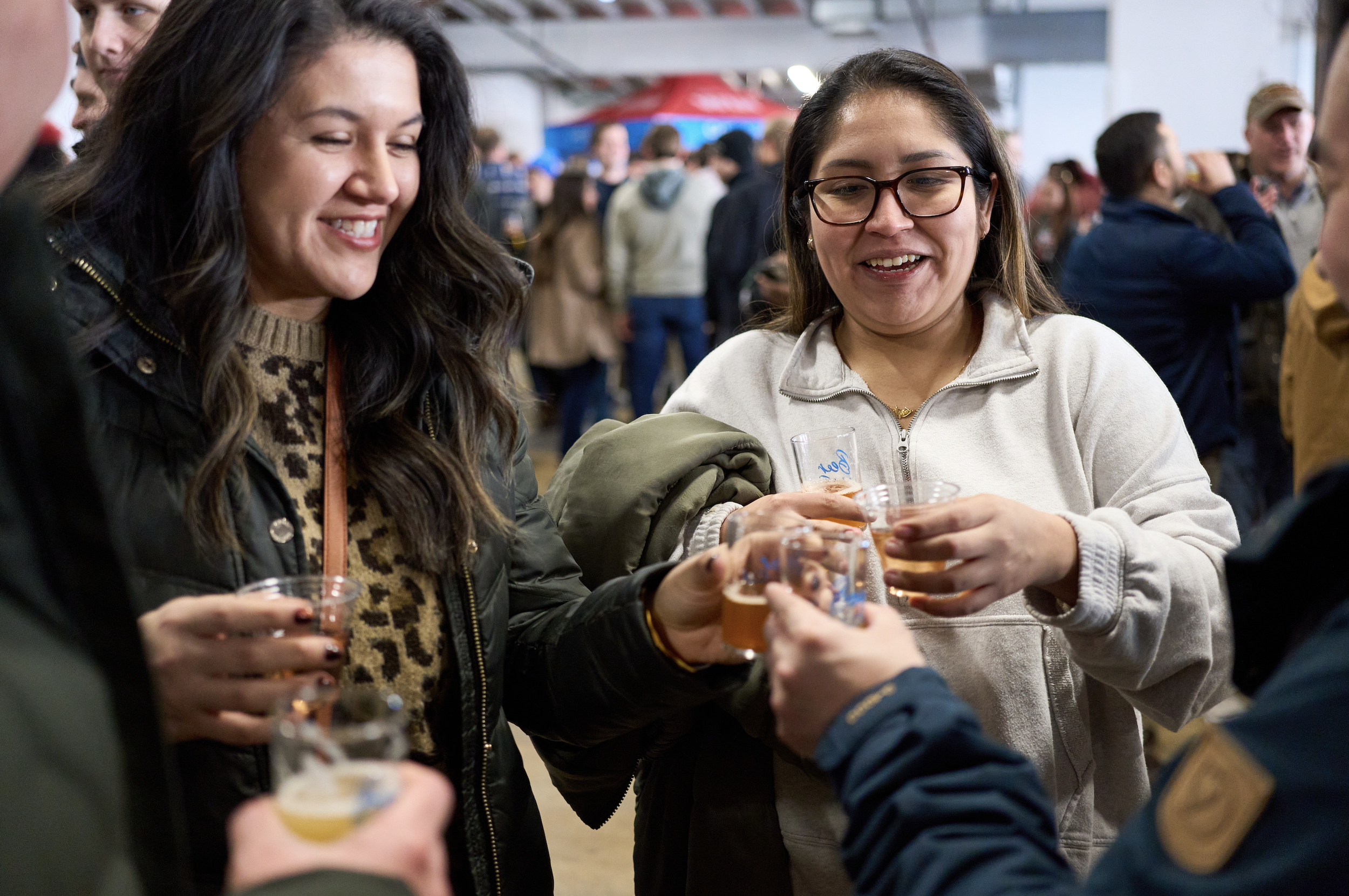 Attendees clinking small beer sample cups together at an indoor beer festival.