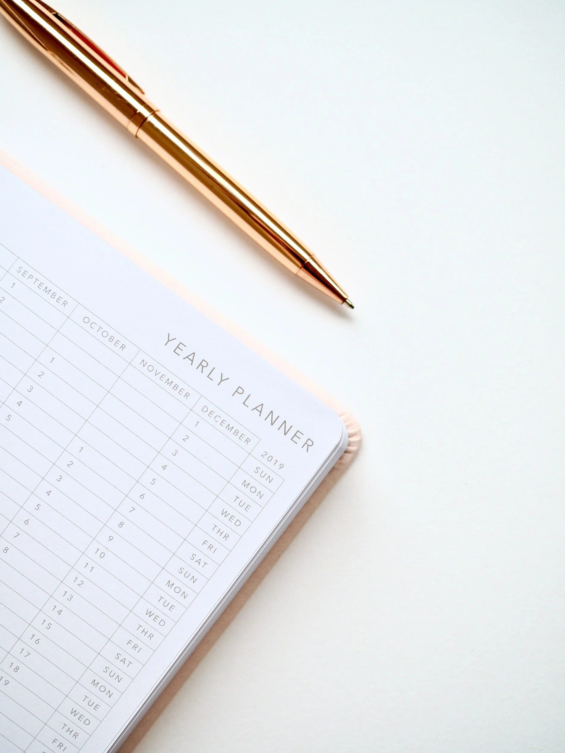 Close-up of a rose gold pen resting on an open yearly planner on a white surface.