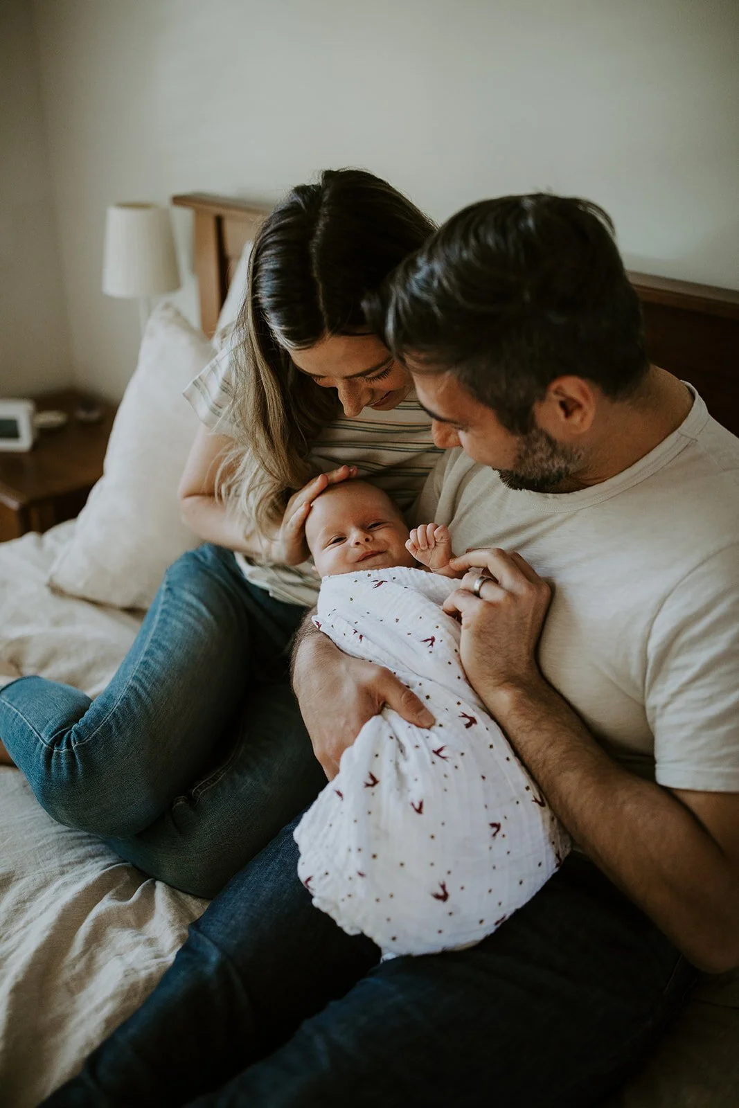 Man+and+woman+sit+together+in+bed+holding+swaddled+baby.jpeg
