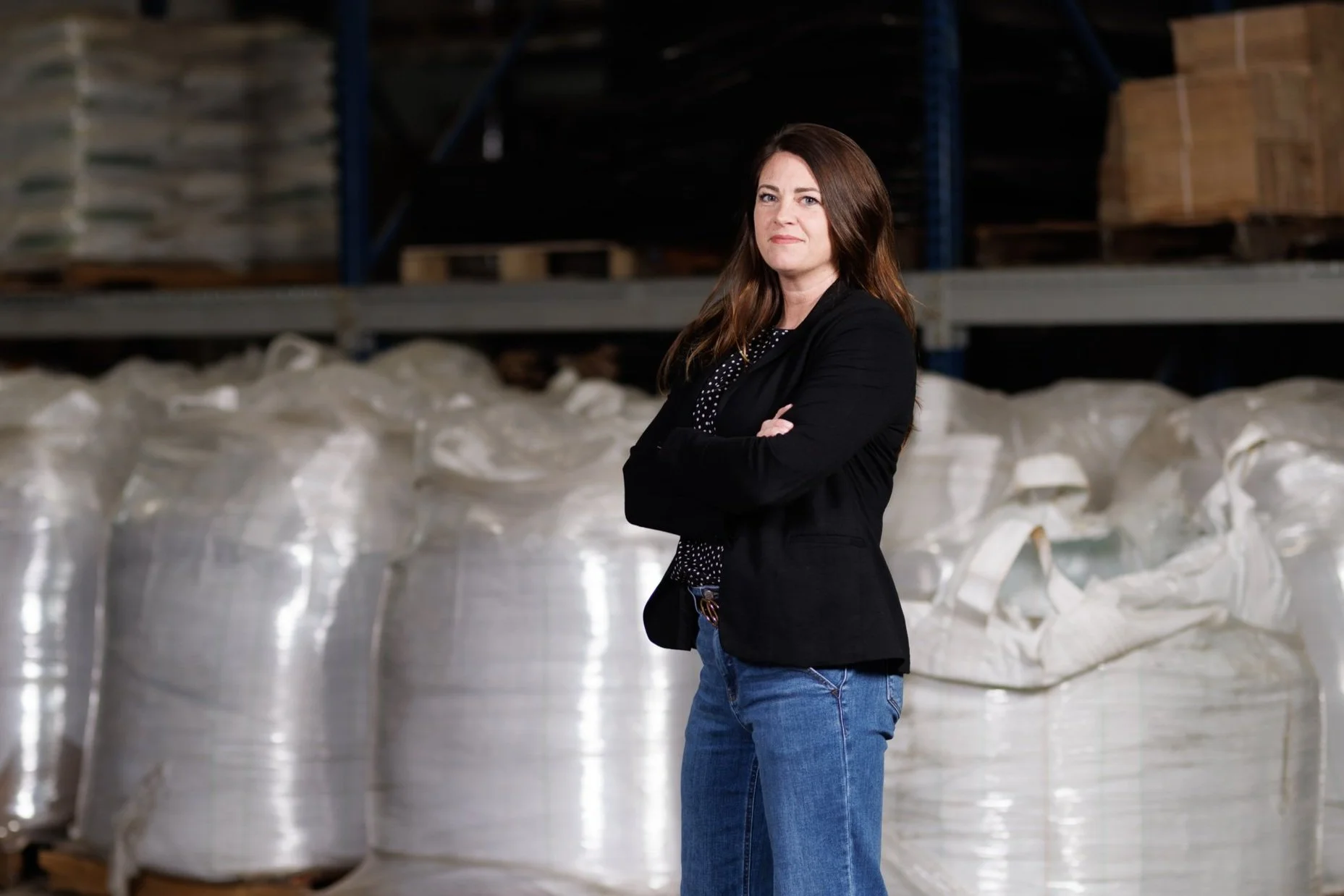 Woman in a warehouse with large white bags and pallets.