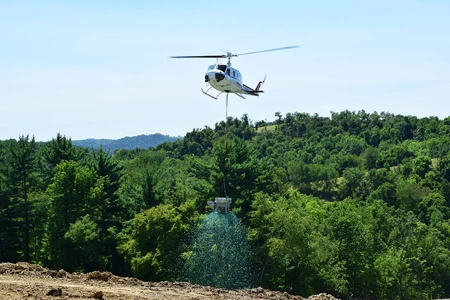 Helicopter spraying seeds over forest landscape