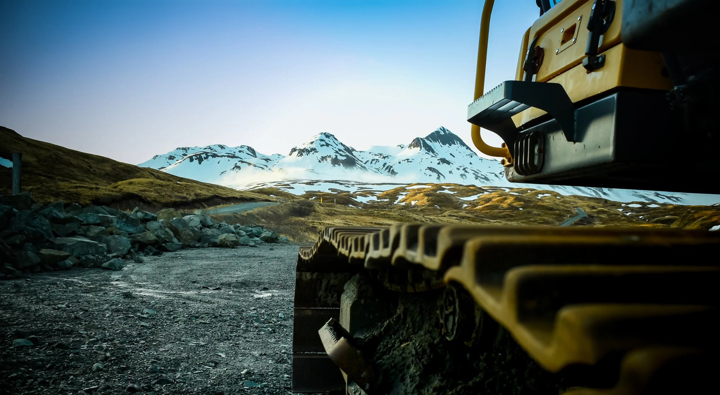 Excavator close-up with snow-covered mountains in the background.