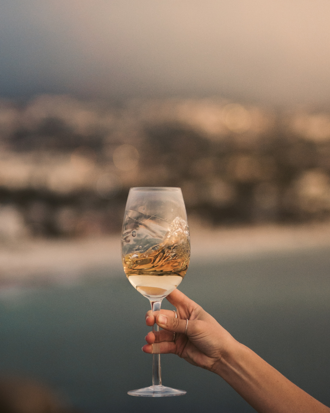 Close up of a wine glass with a blurred coastal background, used to promote a curated wine list for one of the best wine tasting Toronto experiences, featuring Sicily's traditional foods and wines.