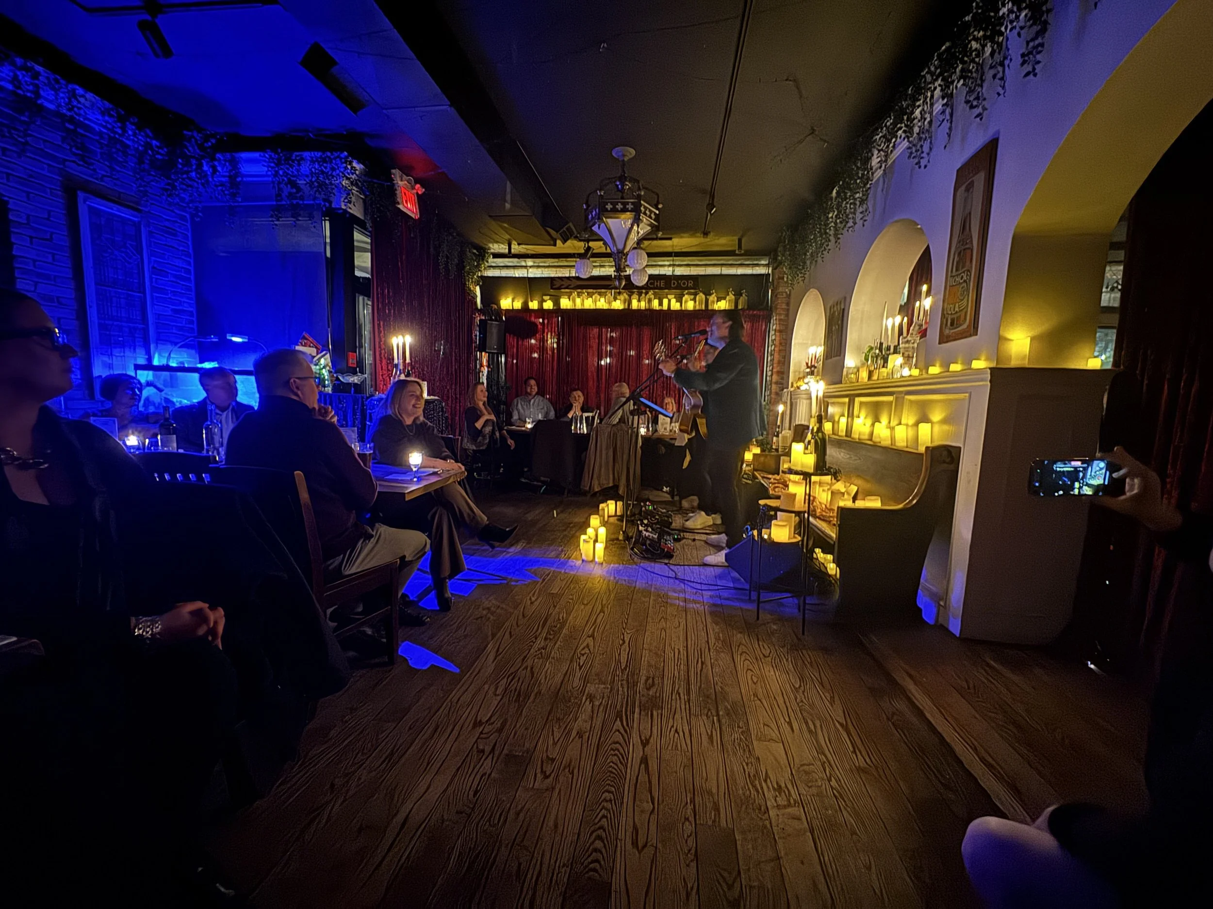 a panoramic view of Desotos Iluminara event on St. Clair West, showing the dining room transformed with red velvet curtains and hundreds of candles. A Beatles tribute performs for a full house at this candlelight concert and three course meal.