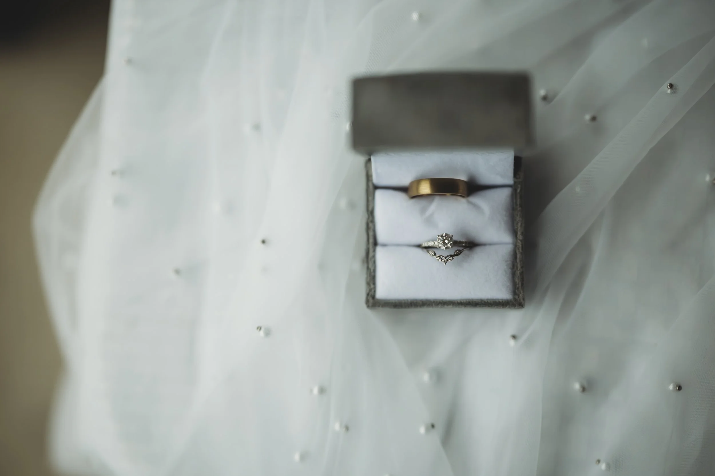 Close-up of two wedding rings in a jewelry box, set against a soft, light-colored background.