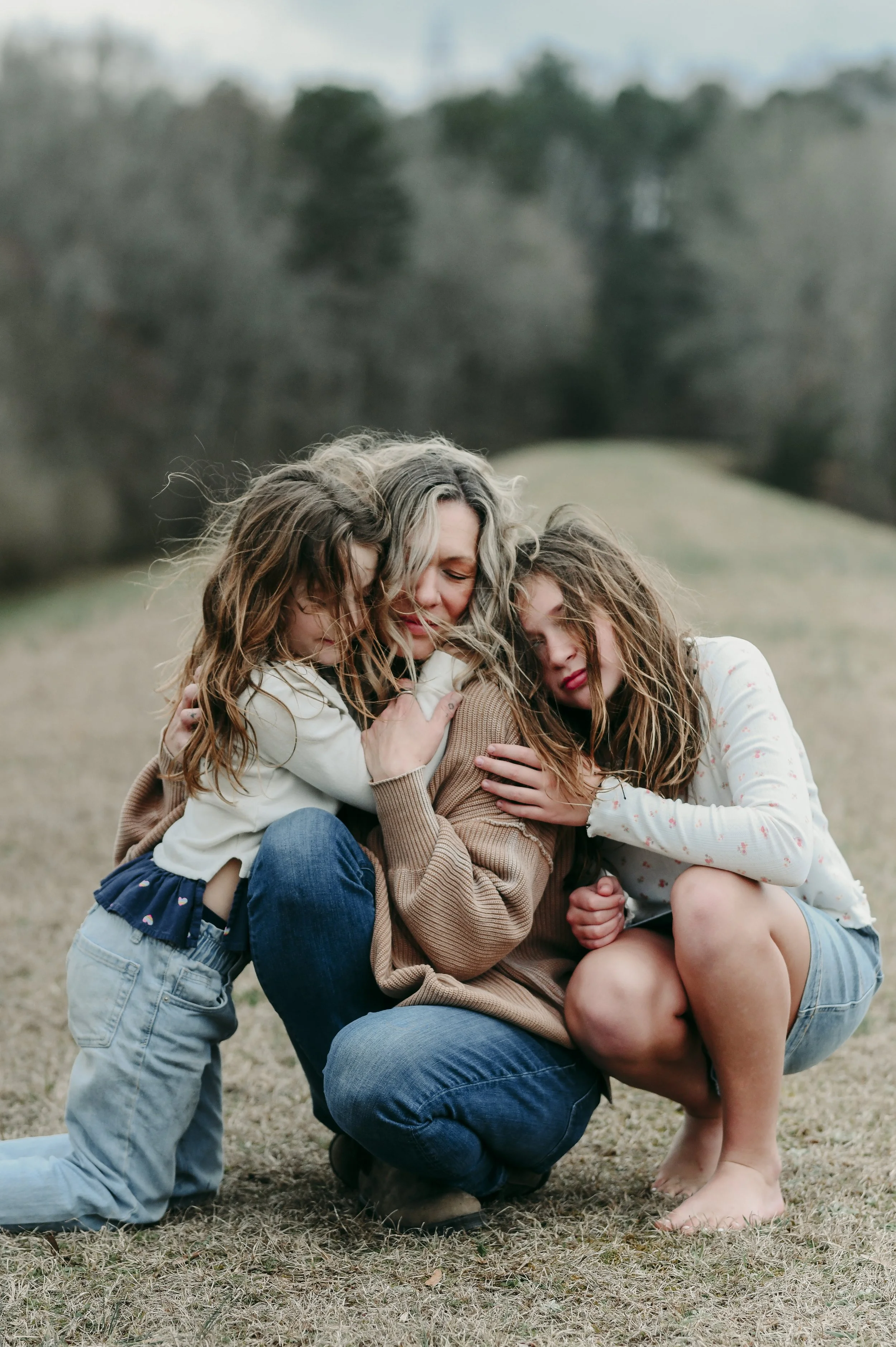 Candid family lifestyle photography of women and a young girl sharing an affectionate moment outdoors.