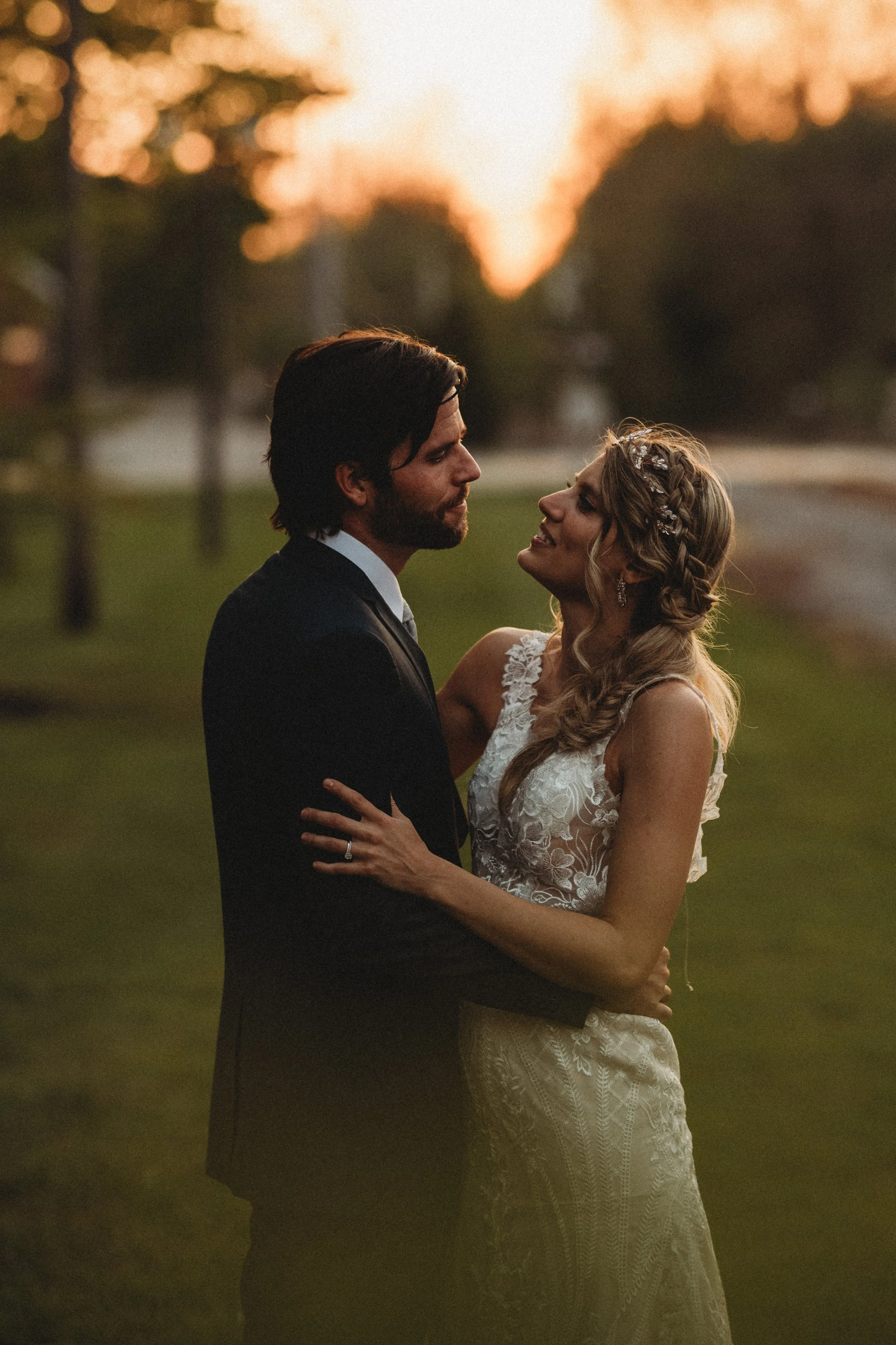 Intimate wedding photography of a bride and groom embracing outdoors at sunset.