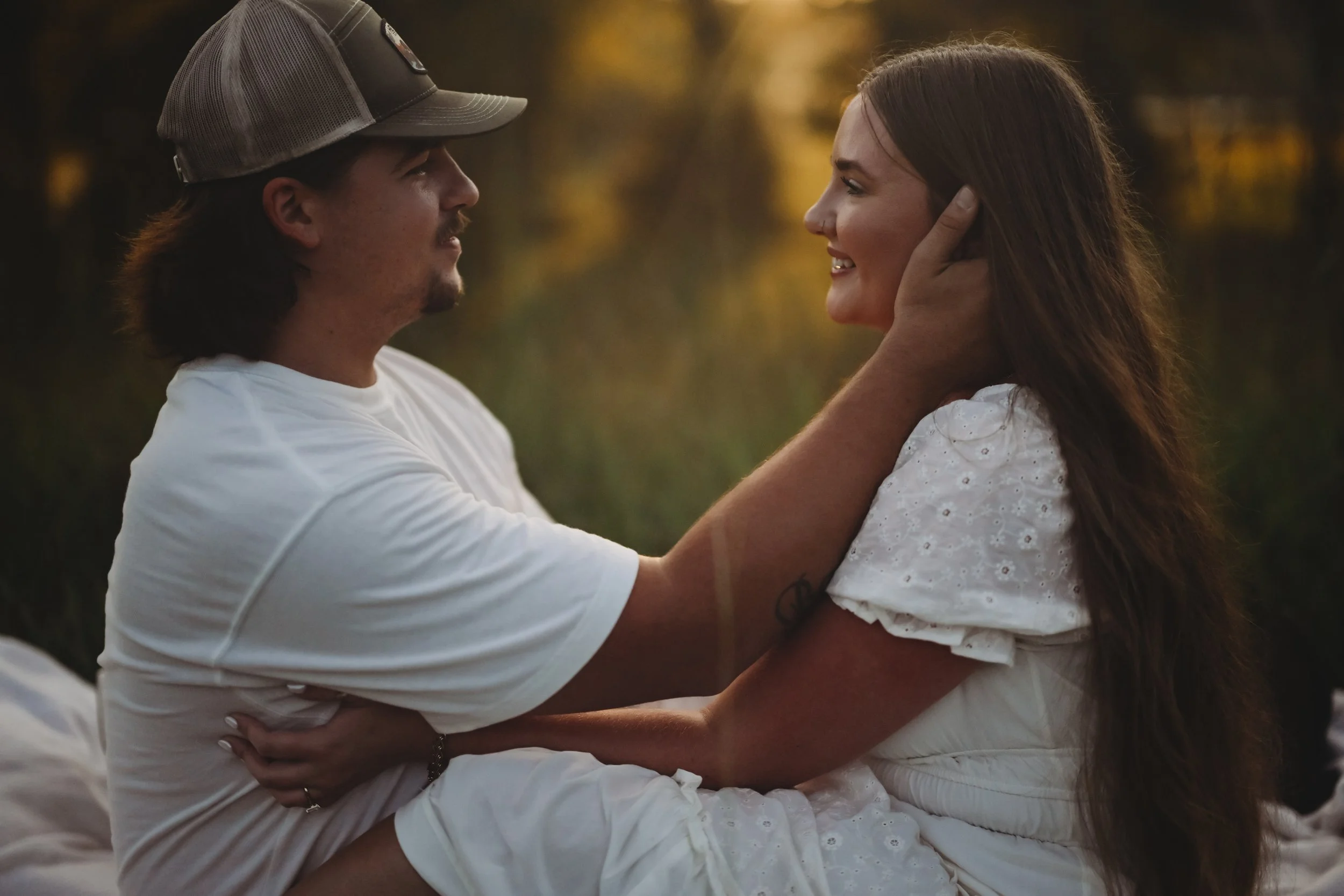 A man and woman are looking at each other with affection; the man is holding the woman's face gently while smiling, and the woman is smiling back.