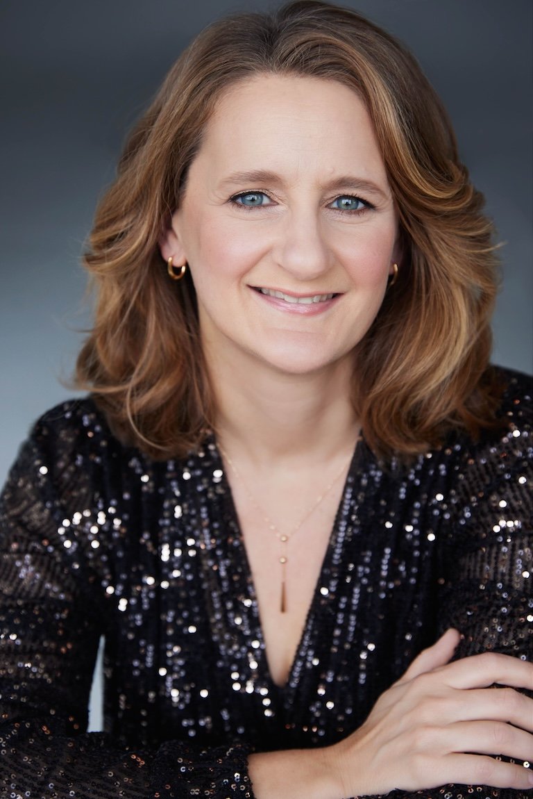 Sophie De Cruz, portant une veste noire en sequins, des boucles d'oreilles or, un collier délicat et posée avec les bras croisés.
