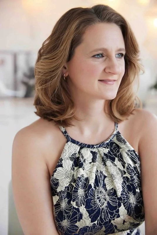 Sophie De Cruz, regarde sur le côté avec un sourire au lèvre. Elle porte une robe fleurit bleu et or.
