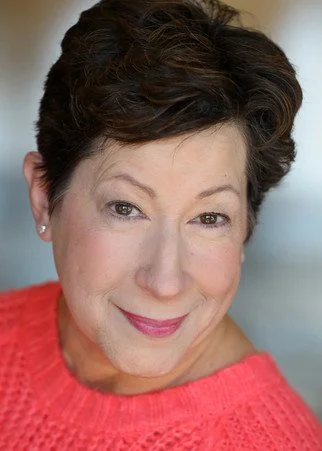 A person with short brown hair wearing a bright pink sweater, smiling at the camera.