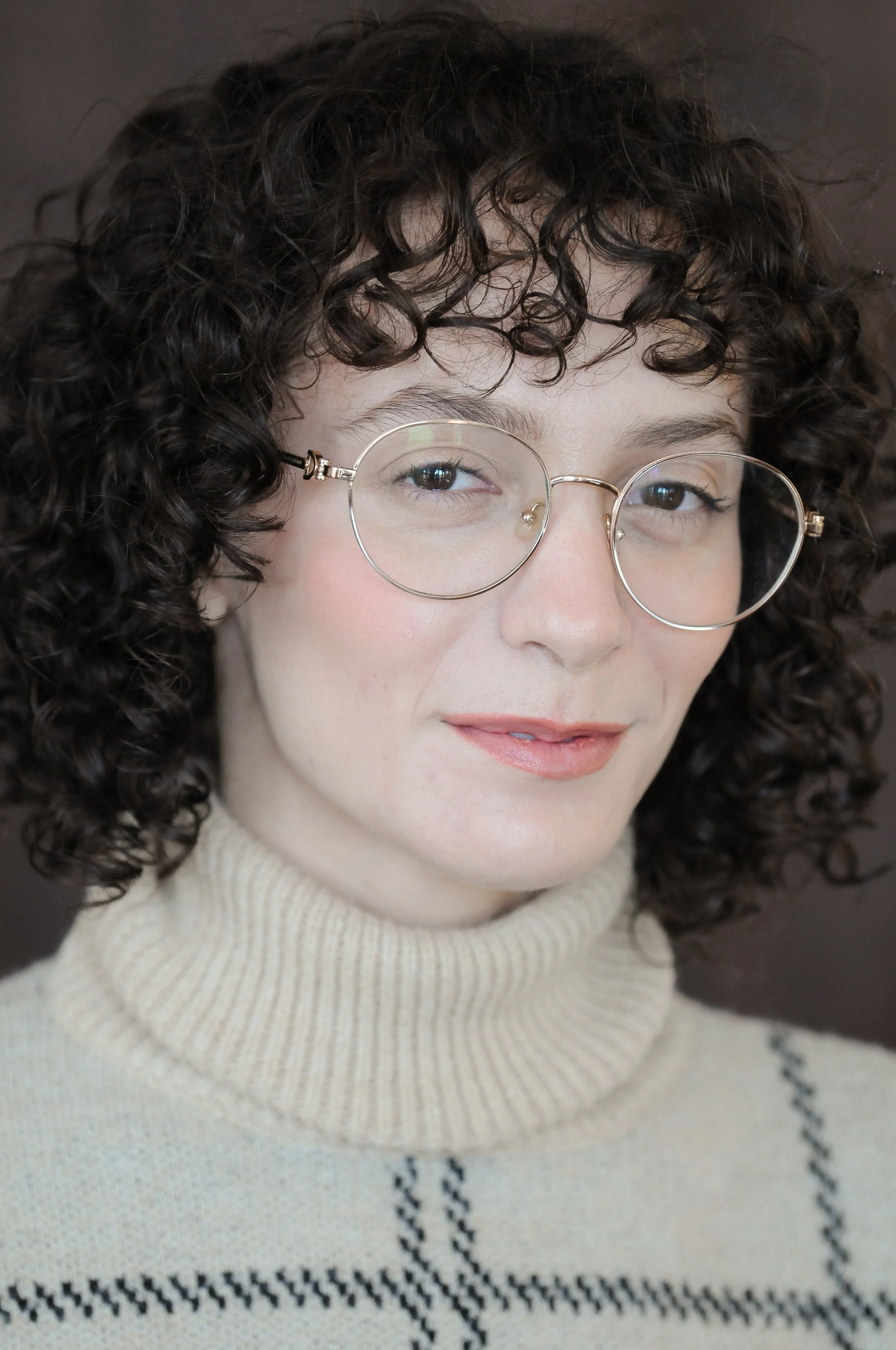 Person with curly hair and glasses wearing a turtleneck sweater