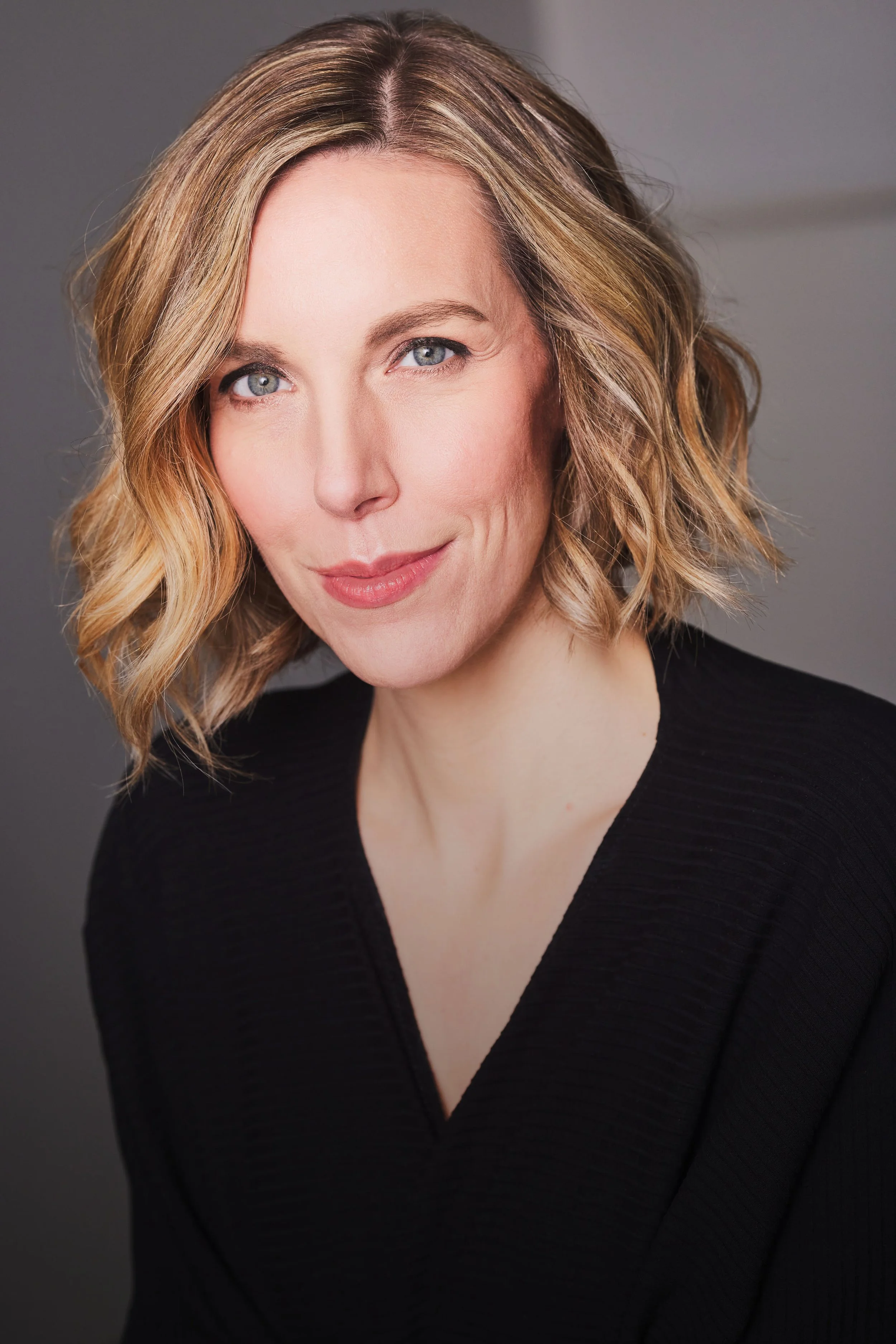 Portrait of a person with short blond hair, wearing a black top, and smiling.