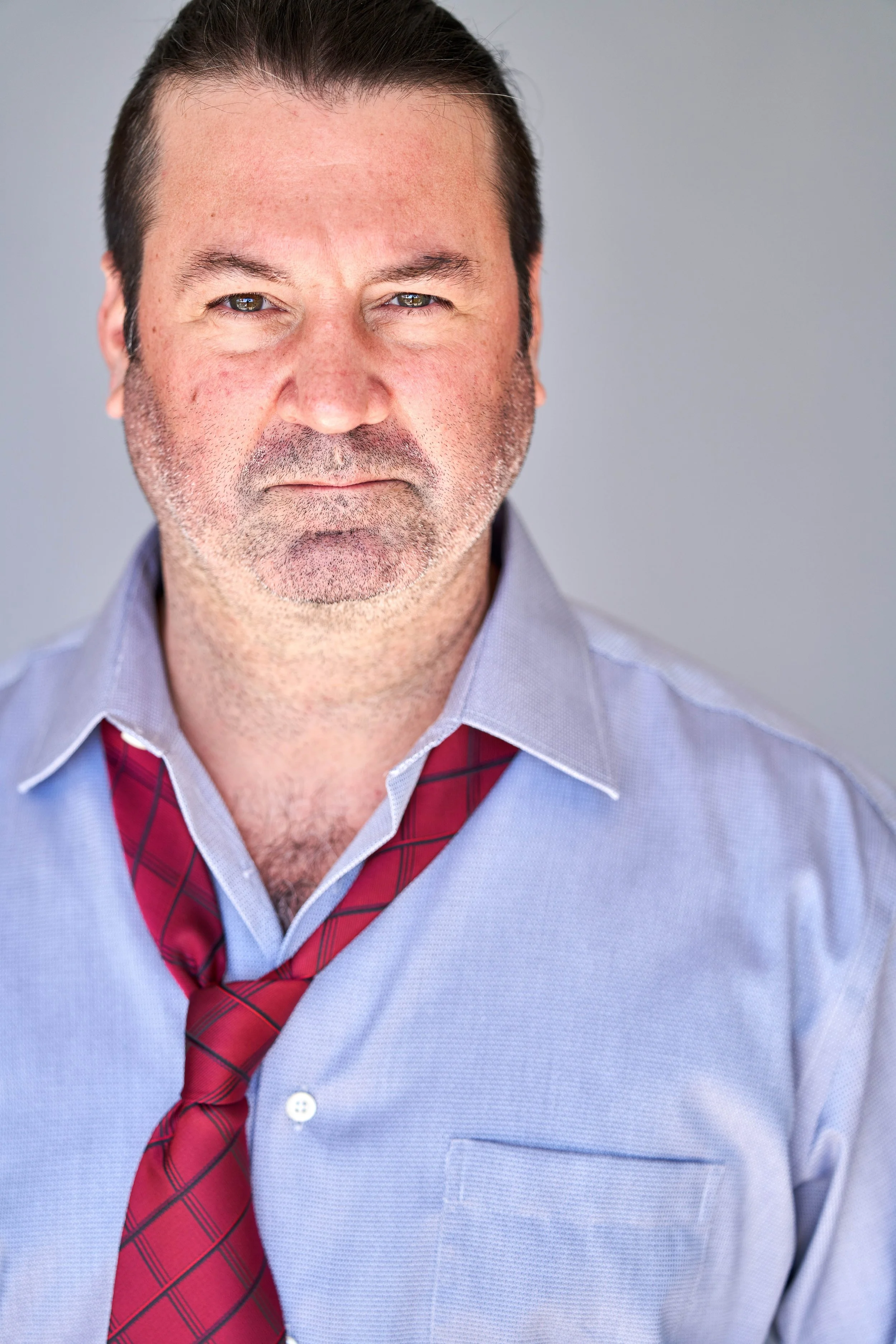 Man with untied red tie and blue shirt, looking serious.