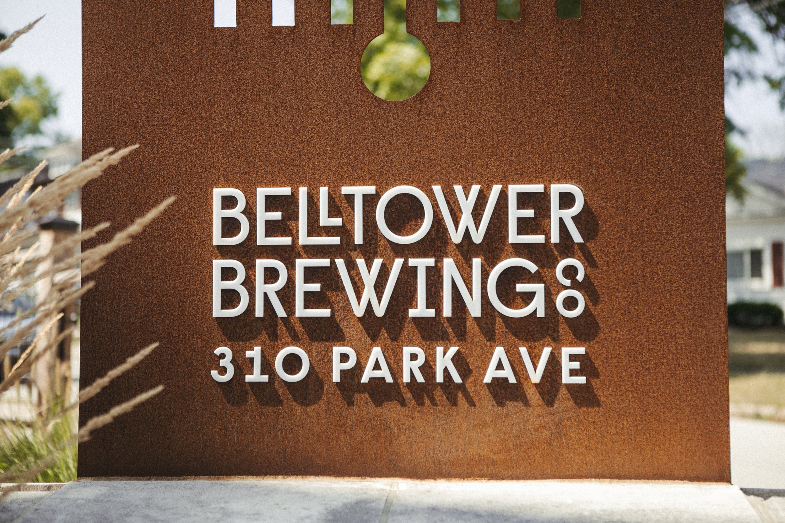 Corten steel sign with white raised lettering reading "BELLTOWER BREWING" and "310 PARK AVE".