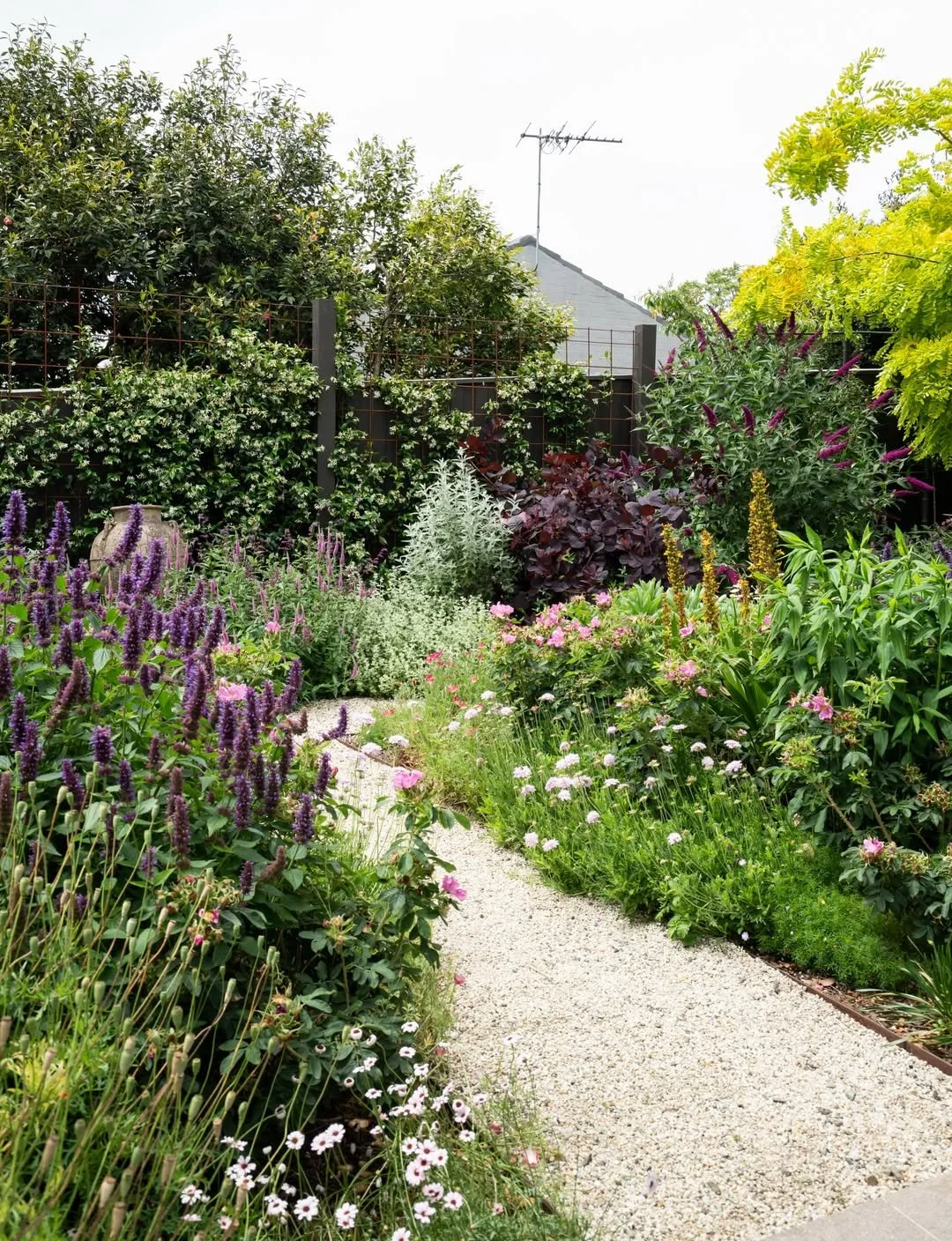 A lush garden with a gravel pathway surrounded by colorful flowers and green foliage.