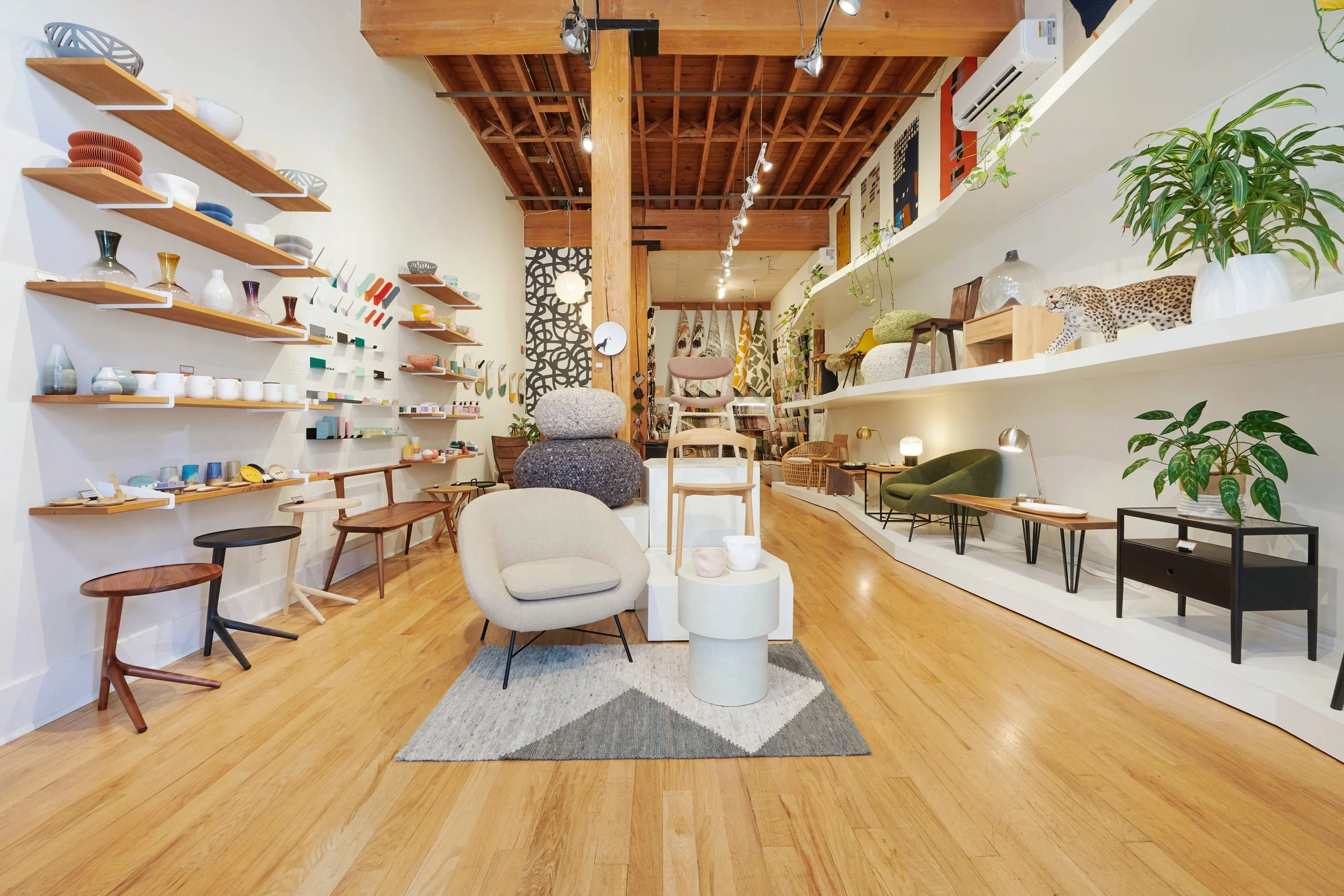 Interior of a modern home decor store featuring wooden floors, white walls, and a variety of furniture and decorative items on shelves and displays, including chairs, plants, and ceramics.