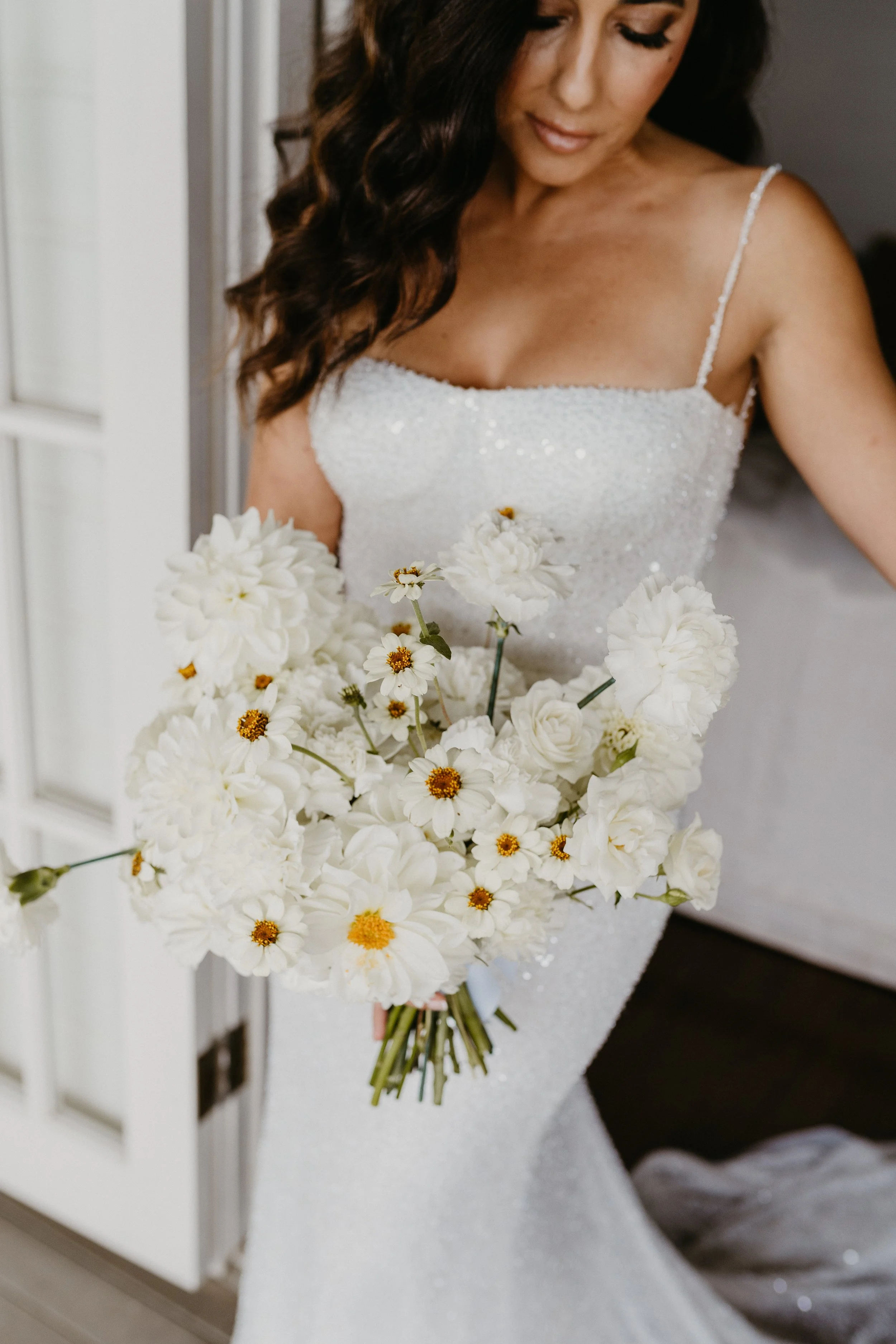A woman in a white wedding dress holding a large bouquet of white flowers.