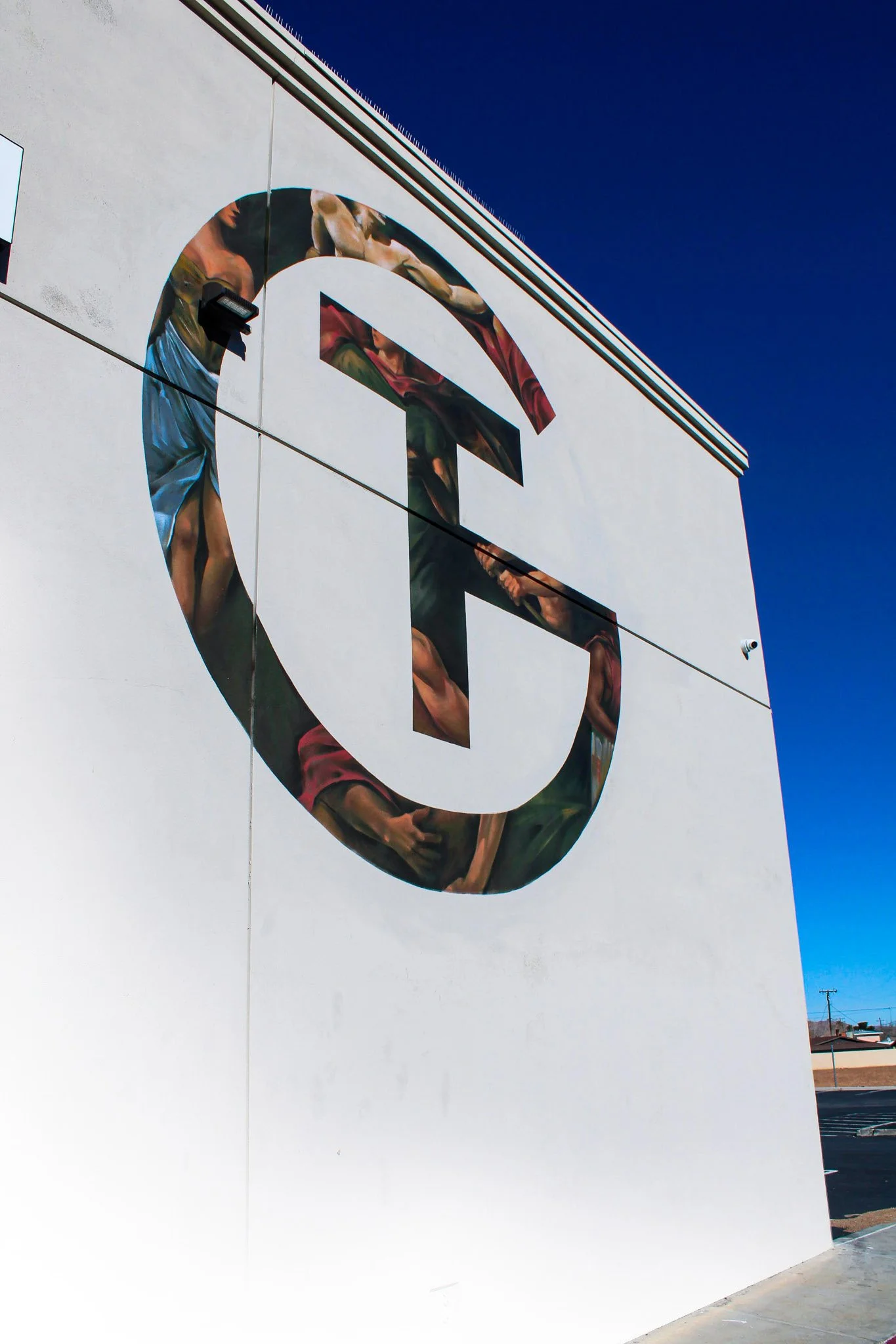 A large white building with a mural of a person in an athletic pose inside a circle. The sky is clear and blue.