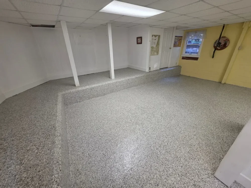 Finished basement with a gray decorative flake floor coating continued over the step-up ledge
