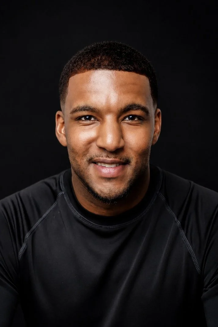 Headshot of a young man with medium skin tone, short curly hair, wearing a black athletic shirt, smiling against a black background.