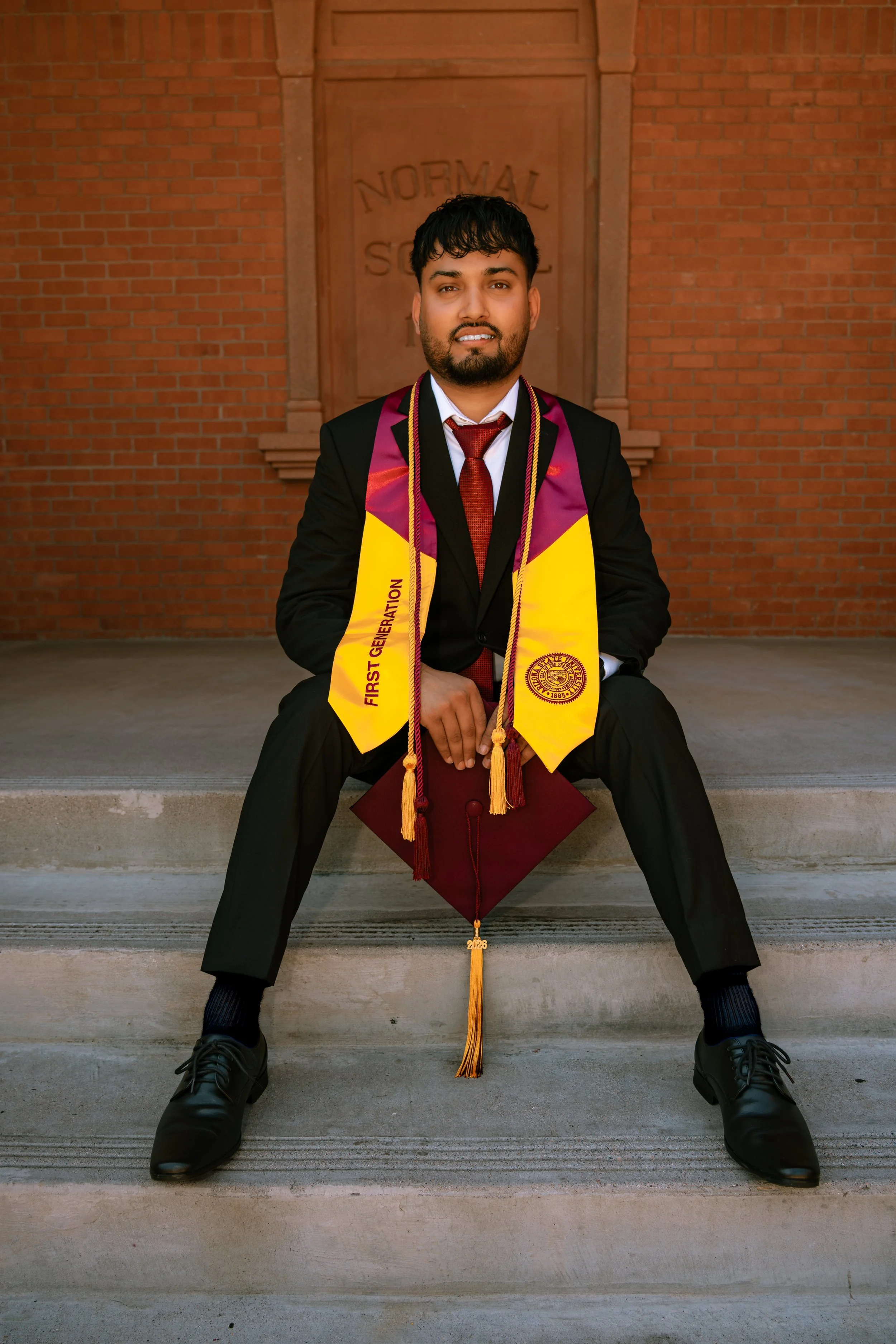 An Arizona State University college graduate sitting on the steps of the Old Main Building in Tempe, AZ